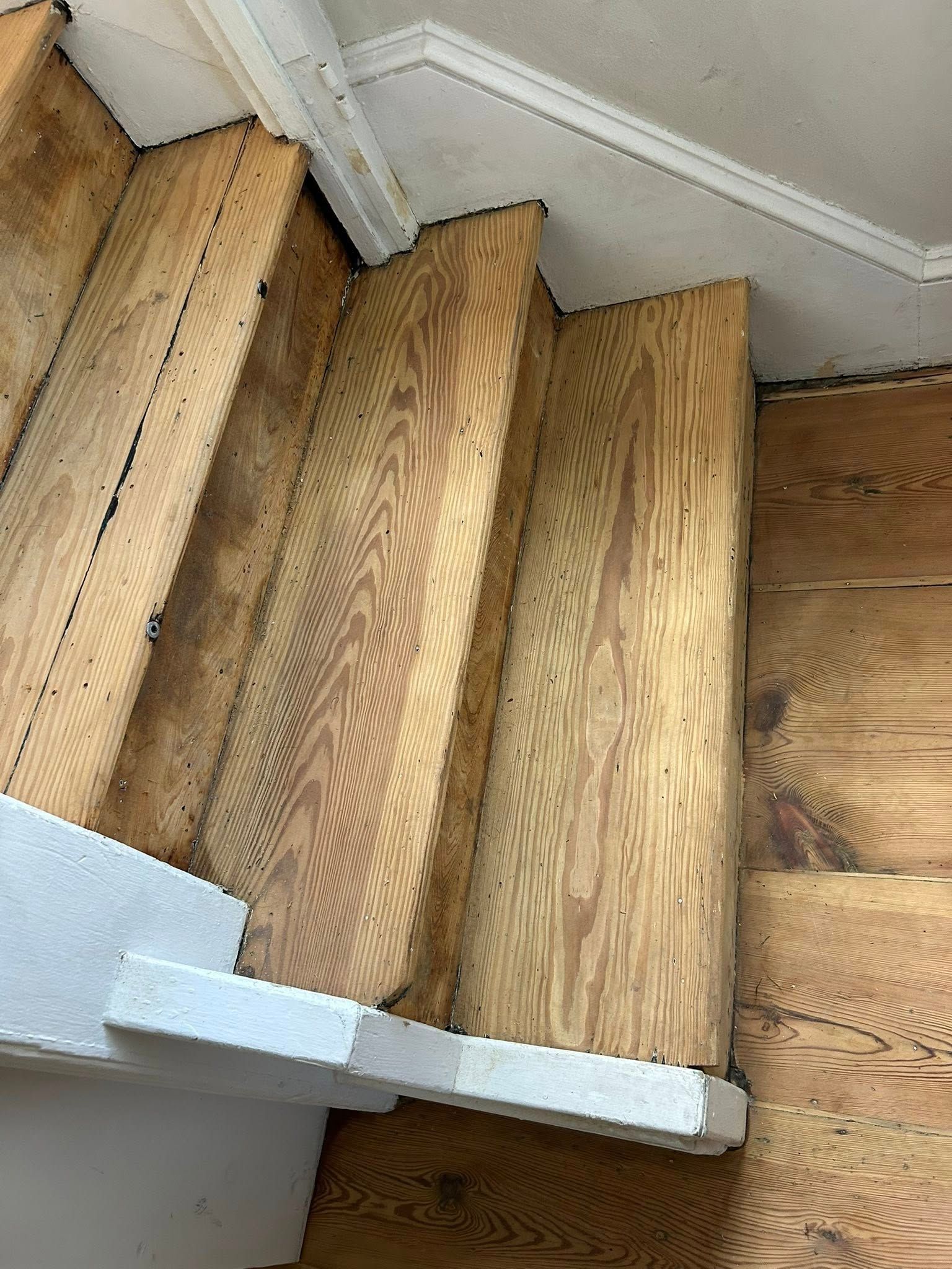 Wooden staircase with worn treads and white trim, viewed from above.