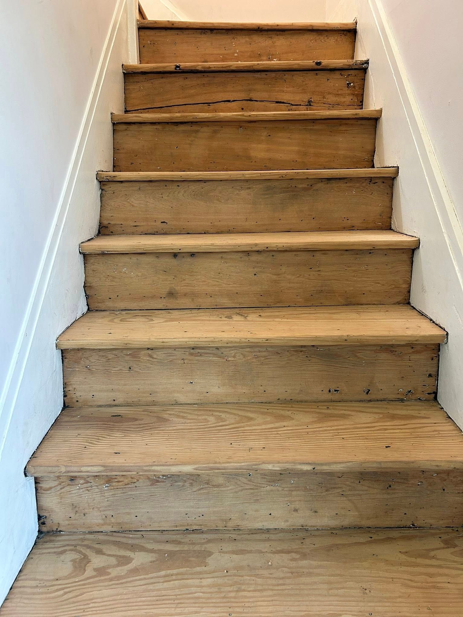 Wooden staircase with worn steps and white walls on either side