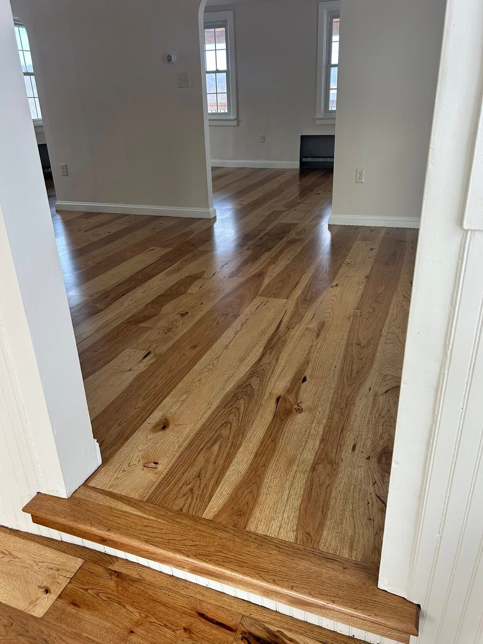 Wooden step down into an empty room with striped hardwood floors and white walls