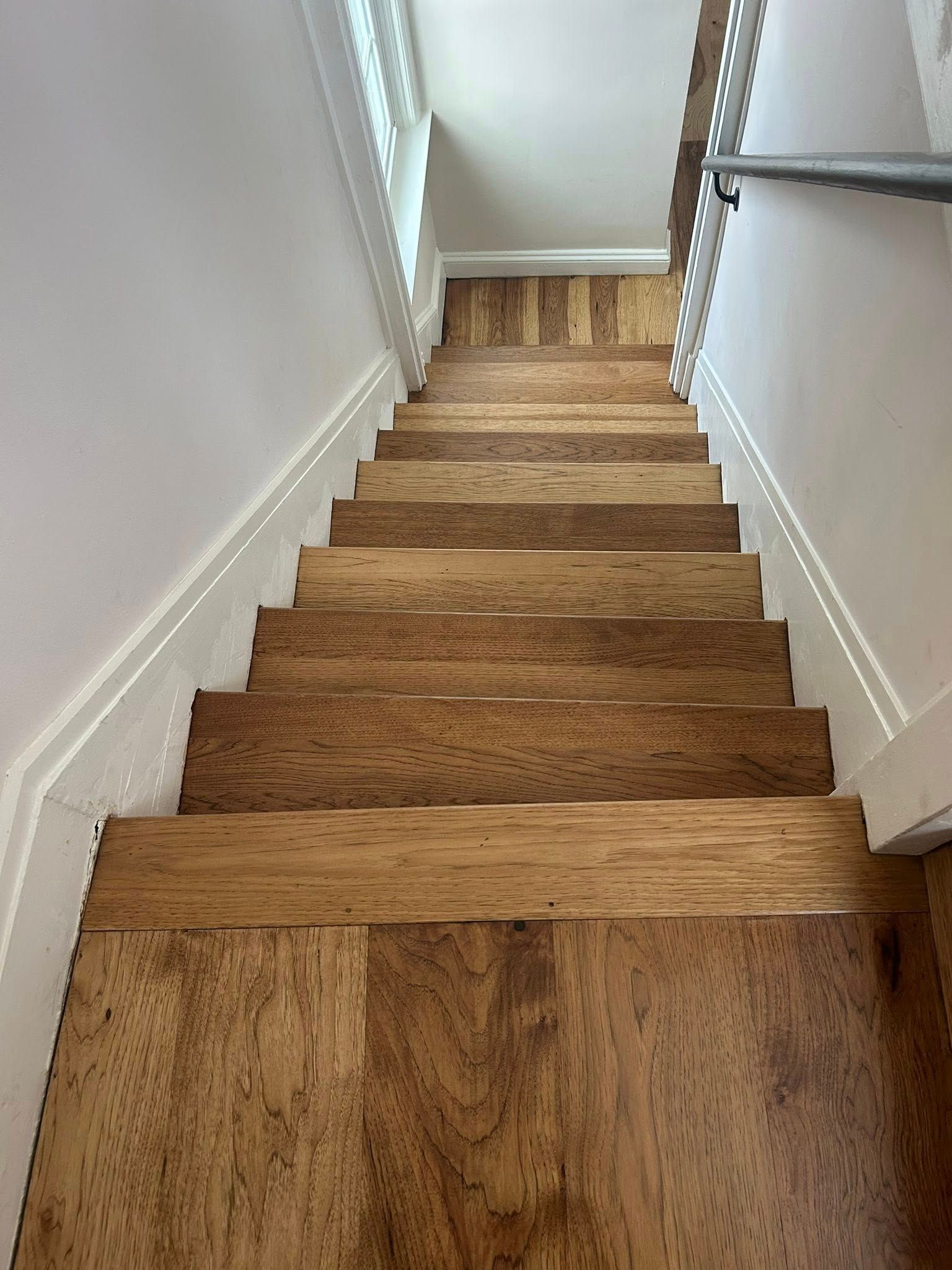 Wooden staircase descending to a hallway, with white walls and a handrail on the right.