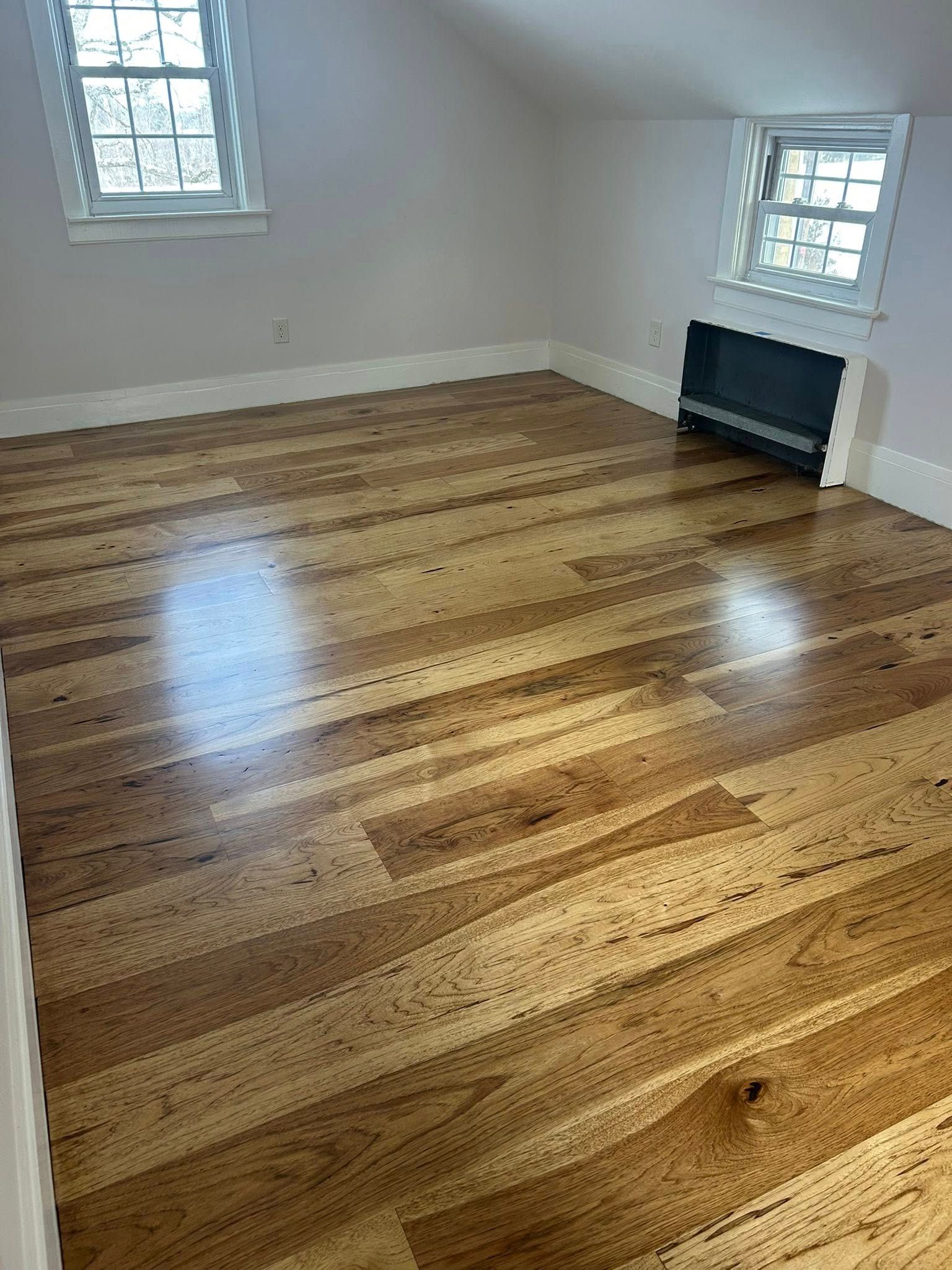 Empty room with polished hardwood floor, white walls, two windows, and a fireplace alcove.