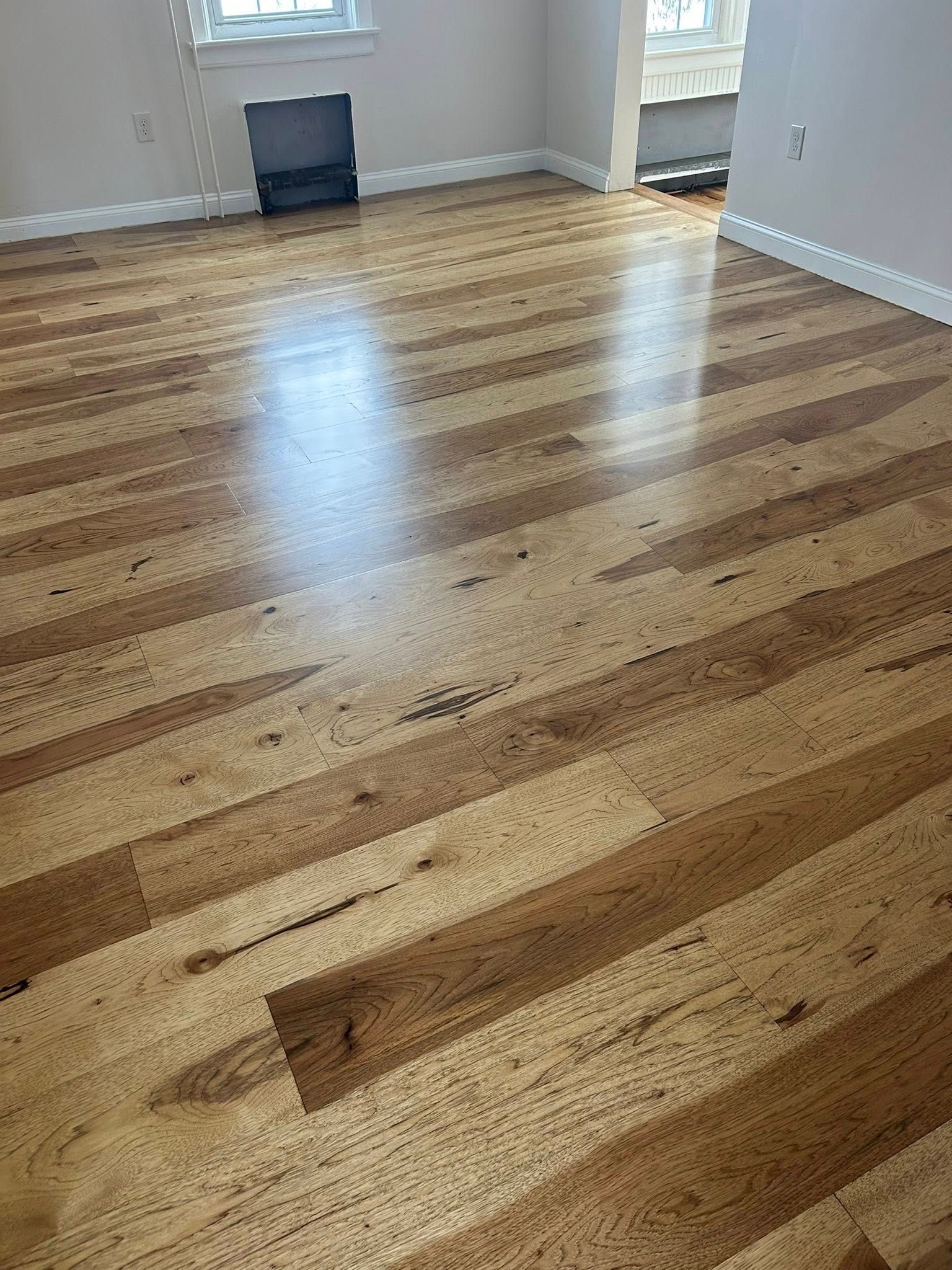 Empty room with newly refinished wooden floor and white walls, sunlight reflecting from windows