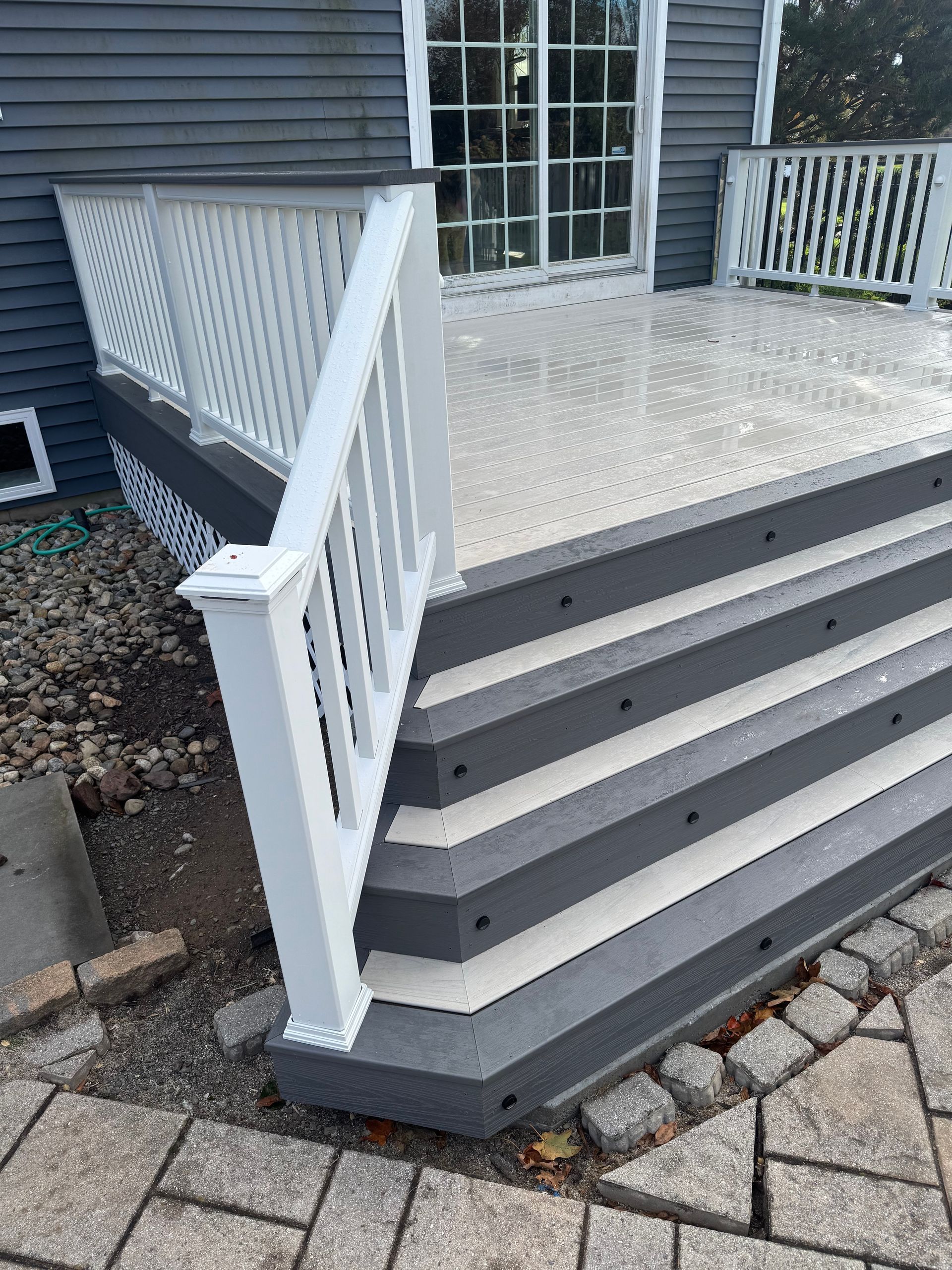 Gray deck with white railing and steps. Building exterior with stone walkway.