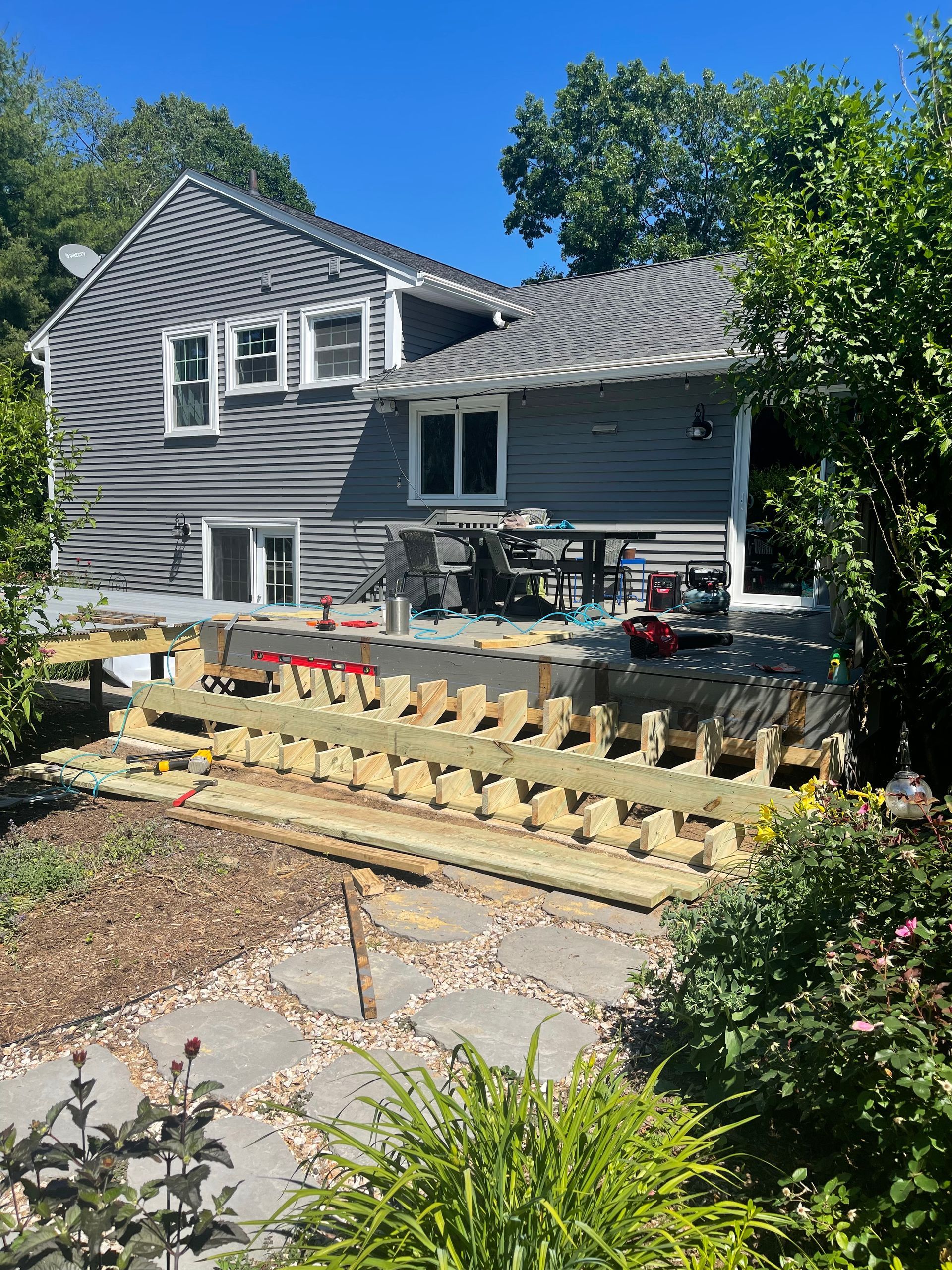 House with new deck construction; unfinished wooden frame. Exterior, sunny day.