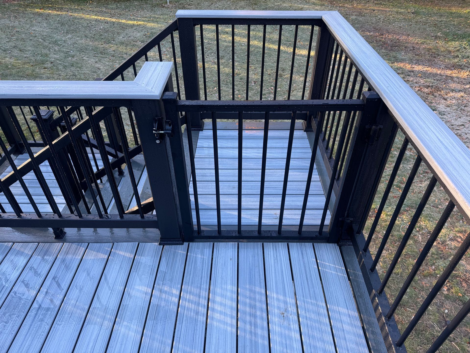 Gray composite deck with black railing and gate, outdoors.