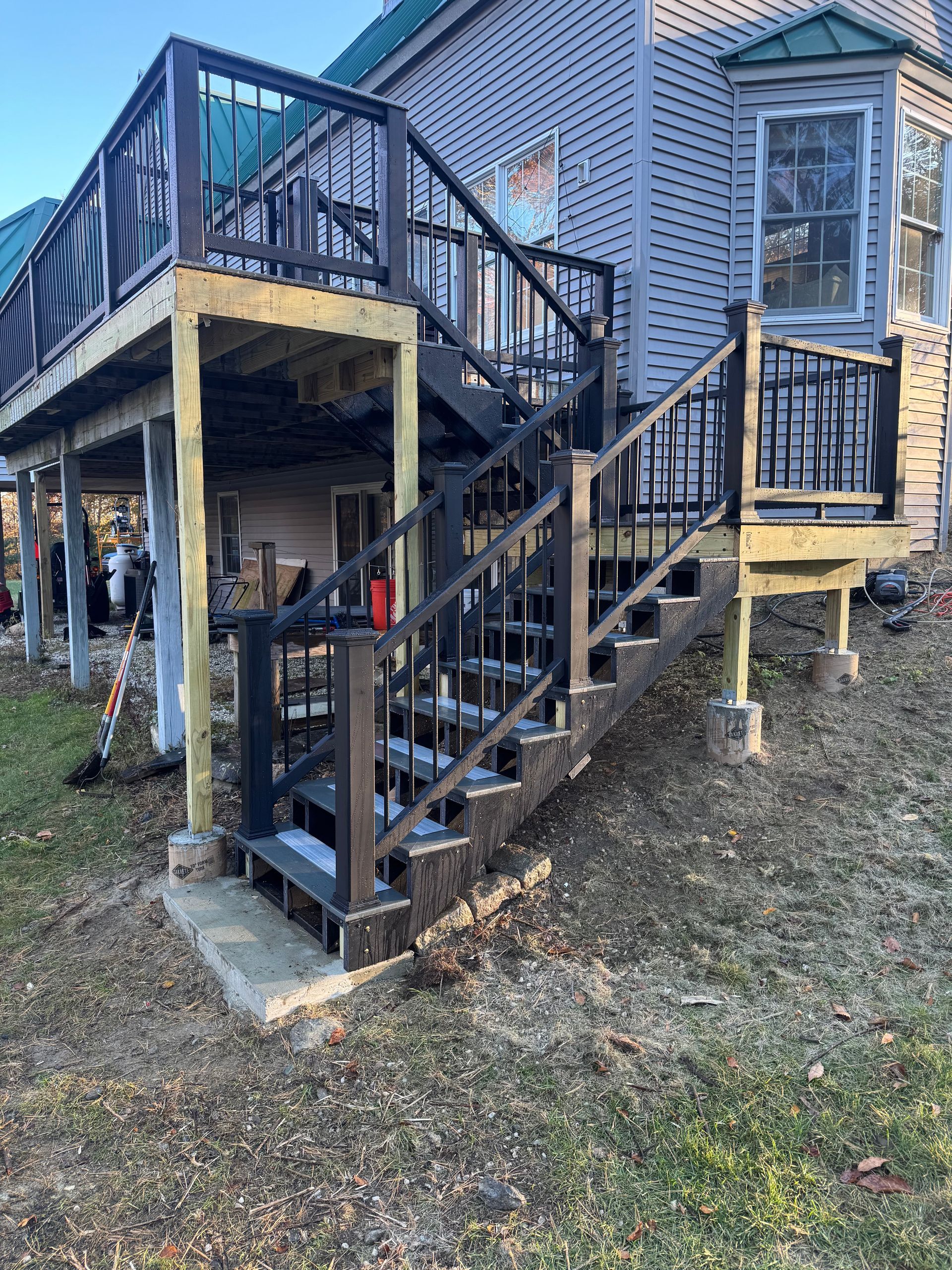 Multi level deck with dark brown railings and stairs attached to a light gray house.