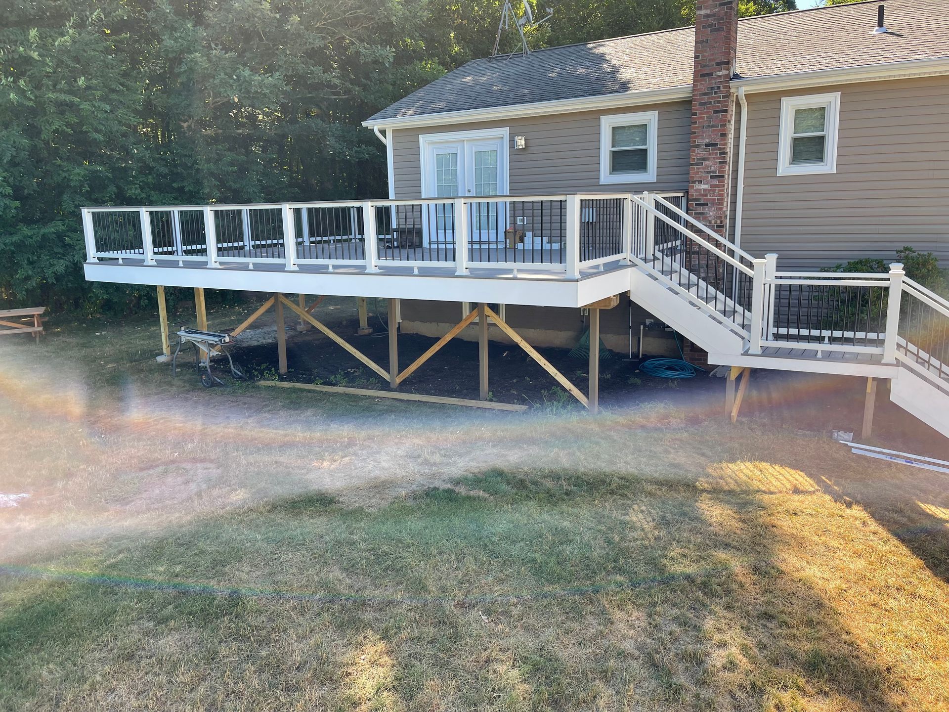 A raised wooden deck attached to a beige house with a staircase. The deck has white and black railings, with grass in front.