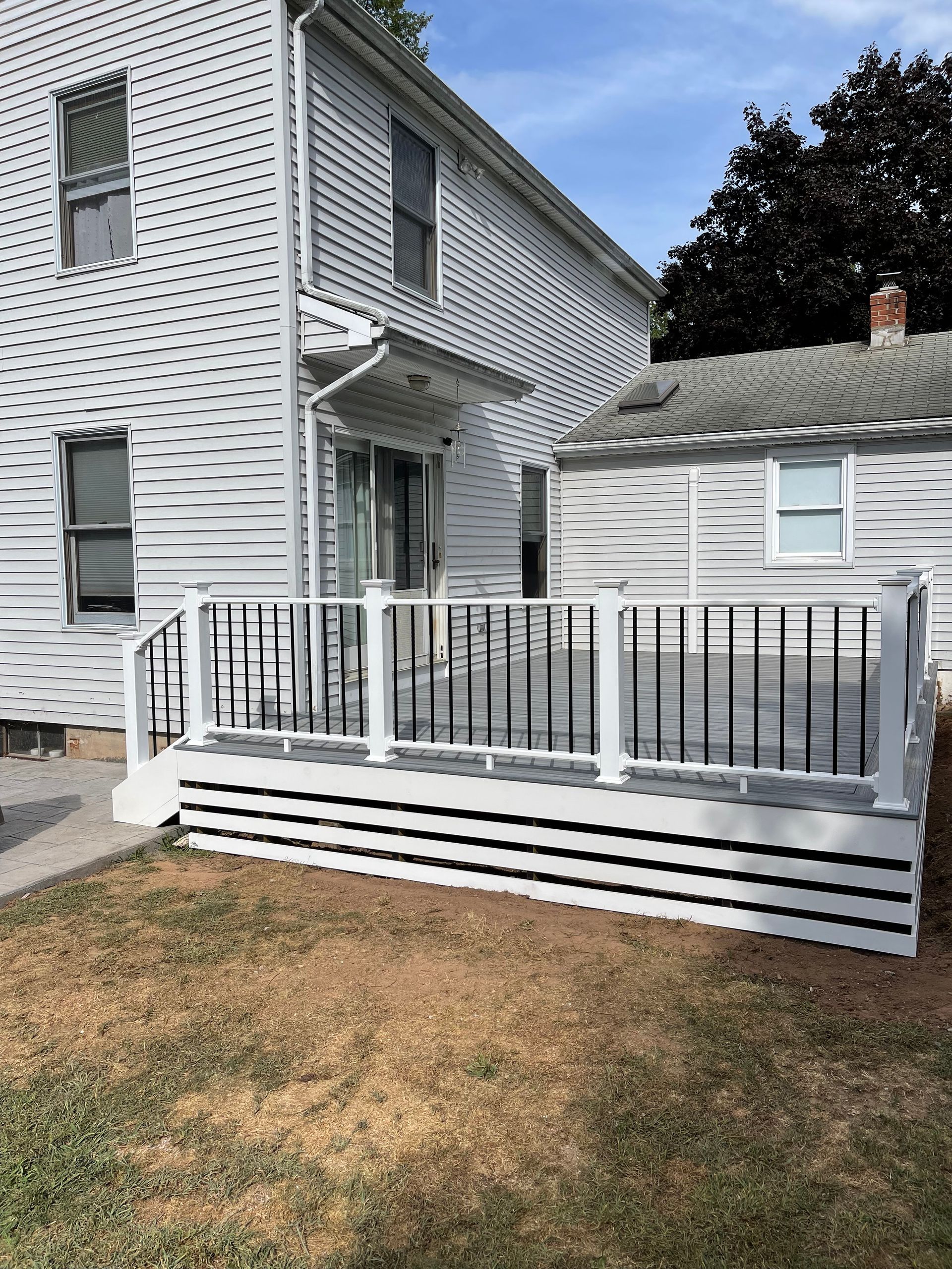 Backyard deck with white and gray railings, connected to a white house.