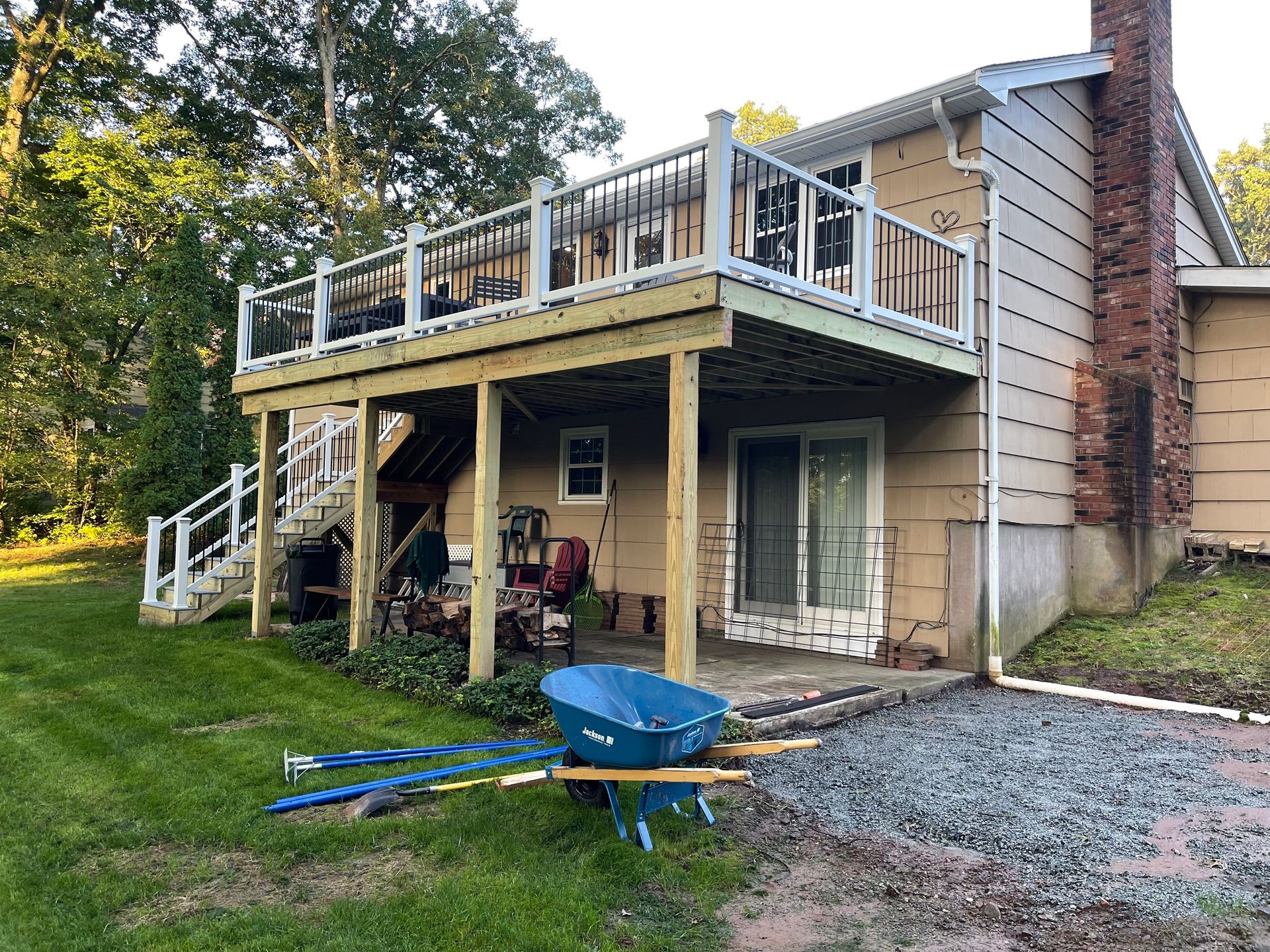 Two-story deck attached to a tan house, with white railing and a wheelbarrow on the grass.
