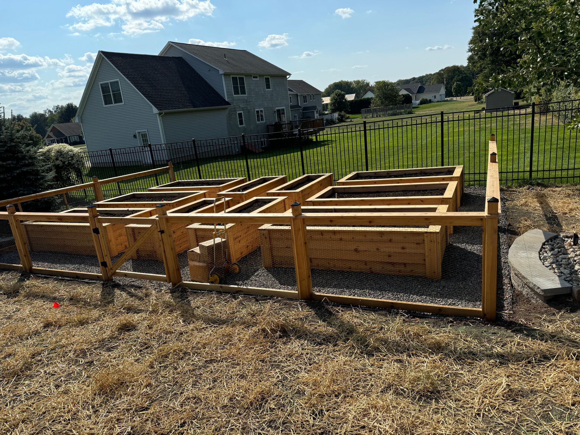 Wooden raised garden beds in a backyard, fenced off with a house and green grass in the background.