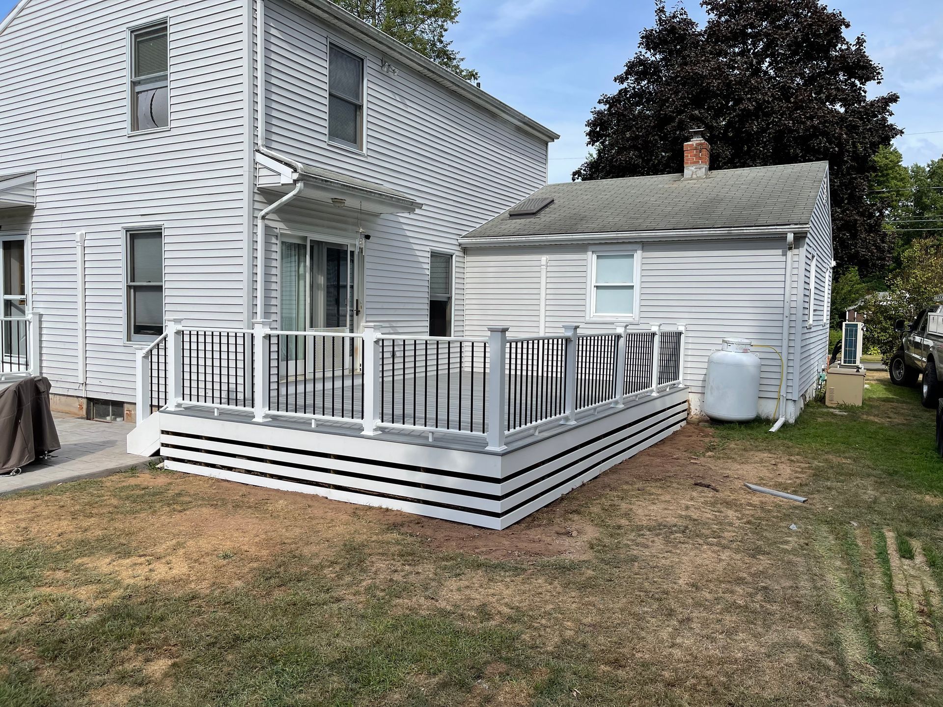 Backyard deck with white railings and trim, adjacent to a white house and small outbuilding.