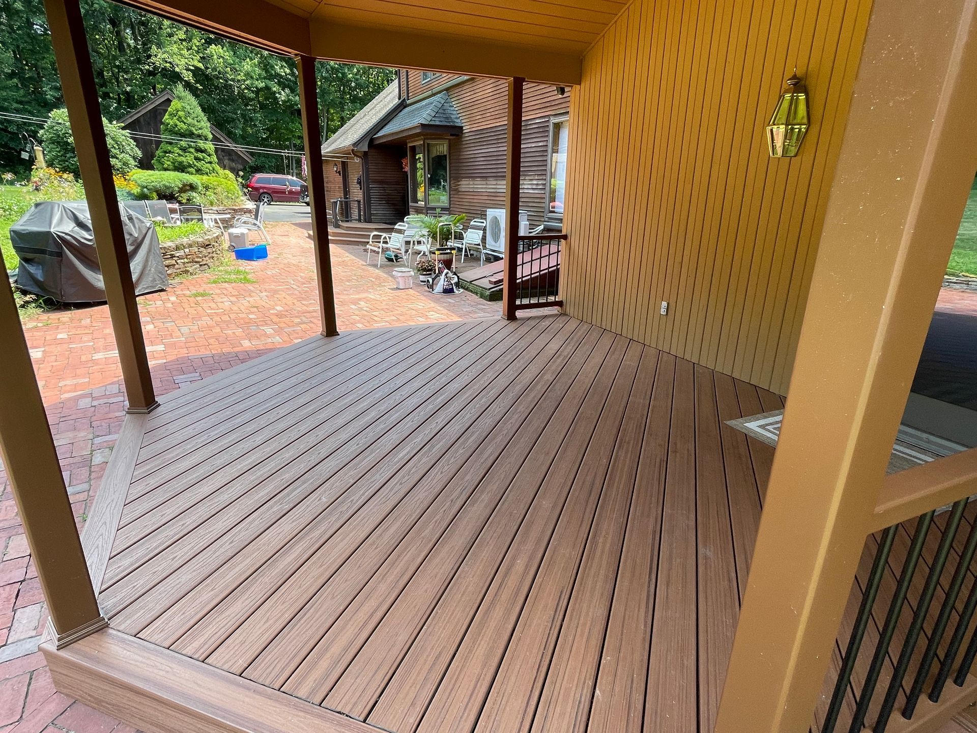 Wooden deck with brown boards, part of a covered patio area. A log cabin in the background.