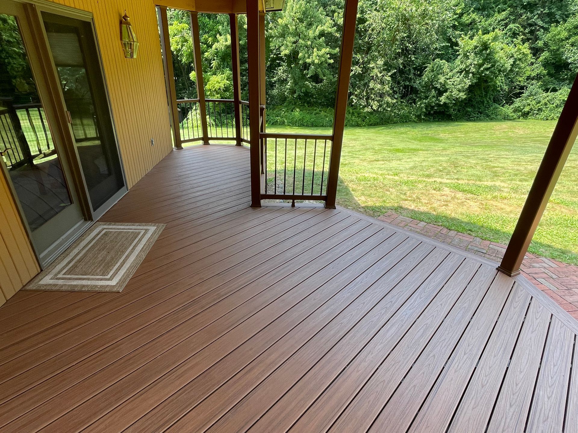 Brown composite deck of a house with a door and grass in the background.