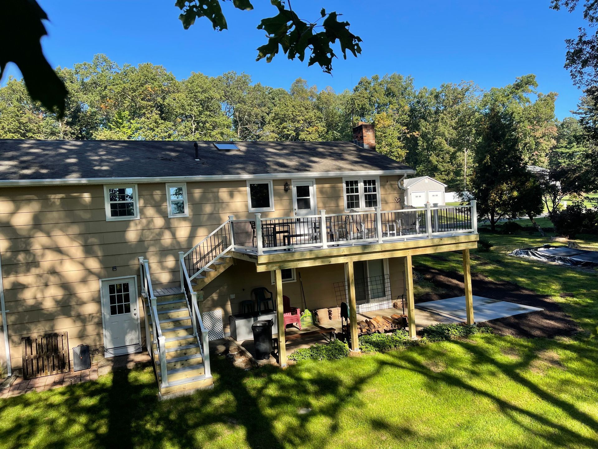 Back of a two-story house with a deck and stairs. The house is beige with green trees in the background.
