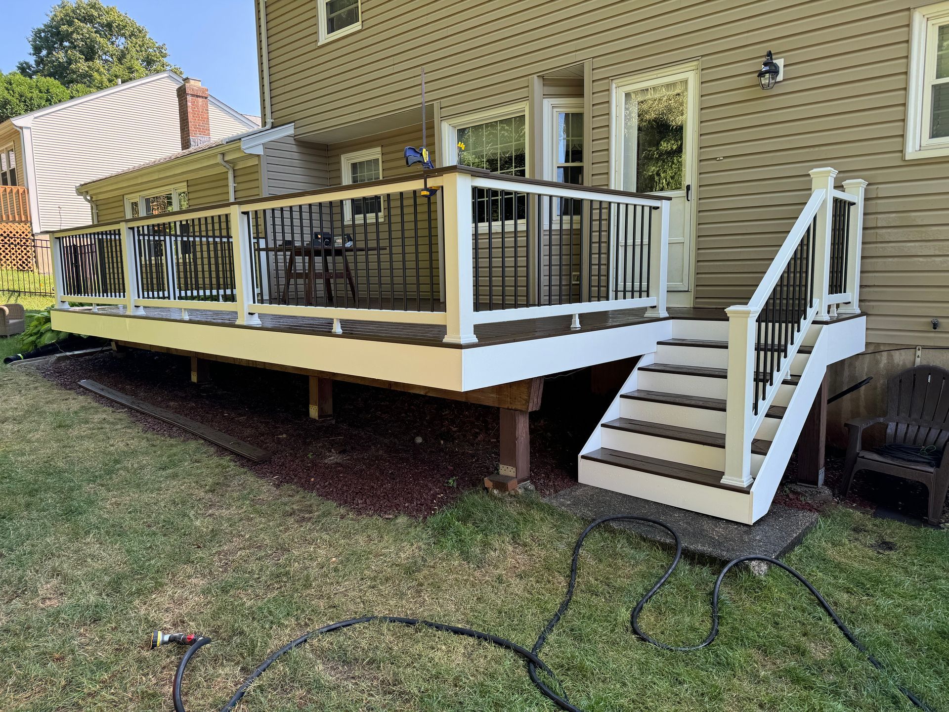 Backyard deck with white and black railings, stairs leading to a door, brown house.