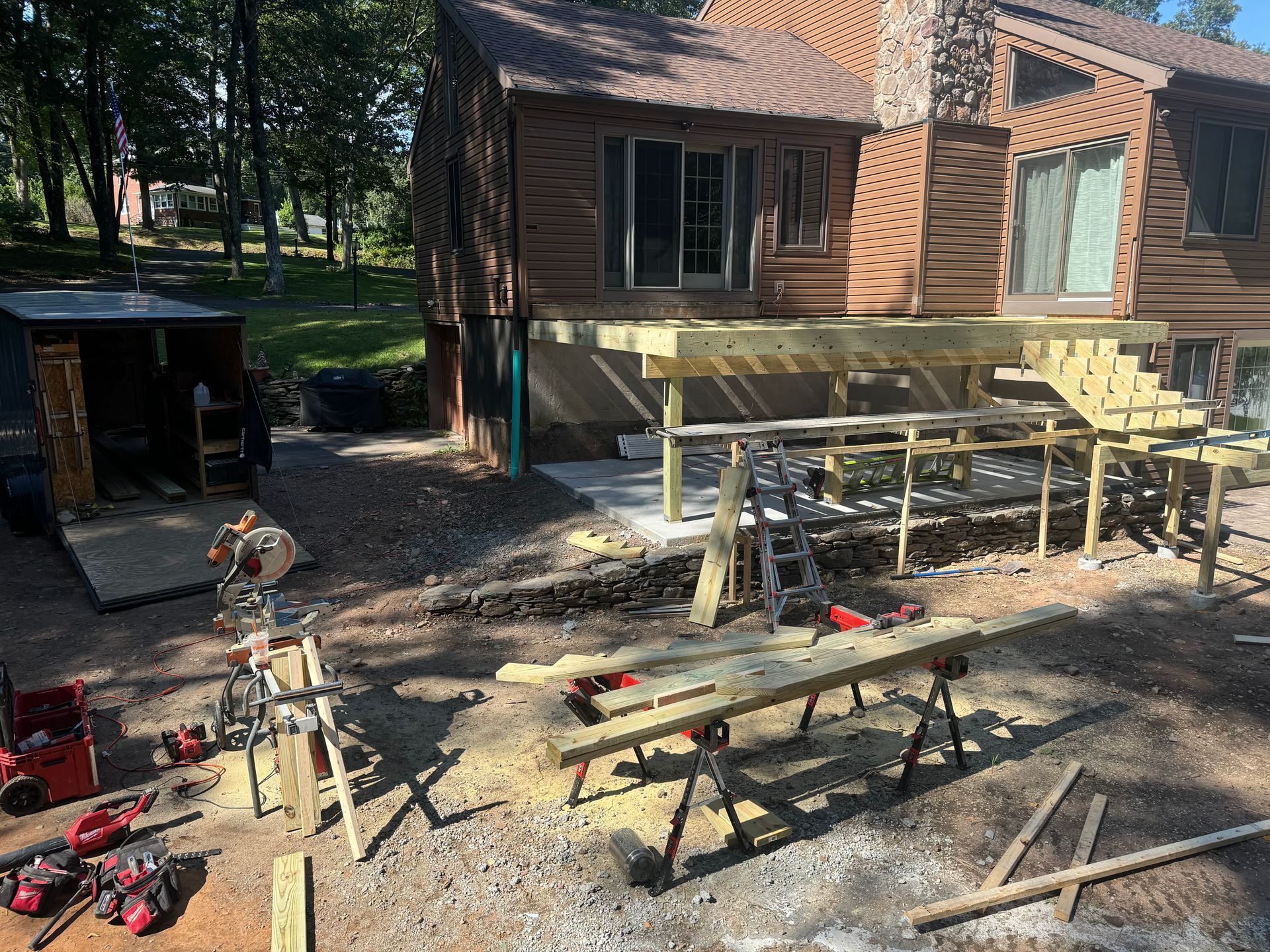 Deck under construction outside a brown house; tools and materials are scattered around.