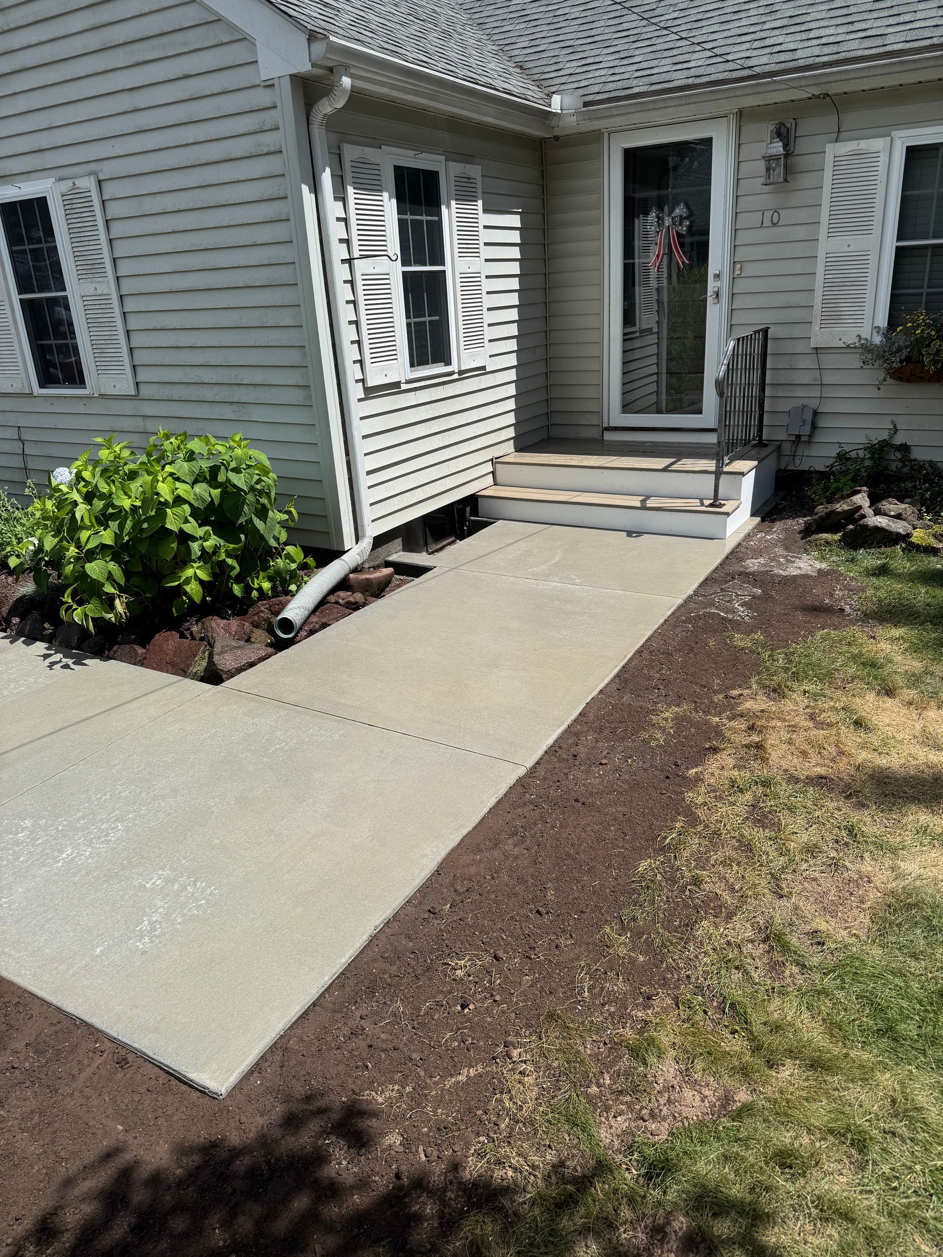 Concrete walkway leads to a house entrance with steps; flanked by mulch beds and grass.