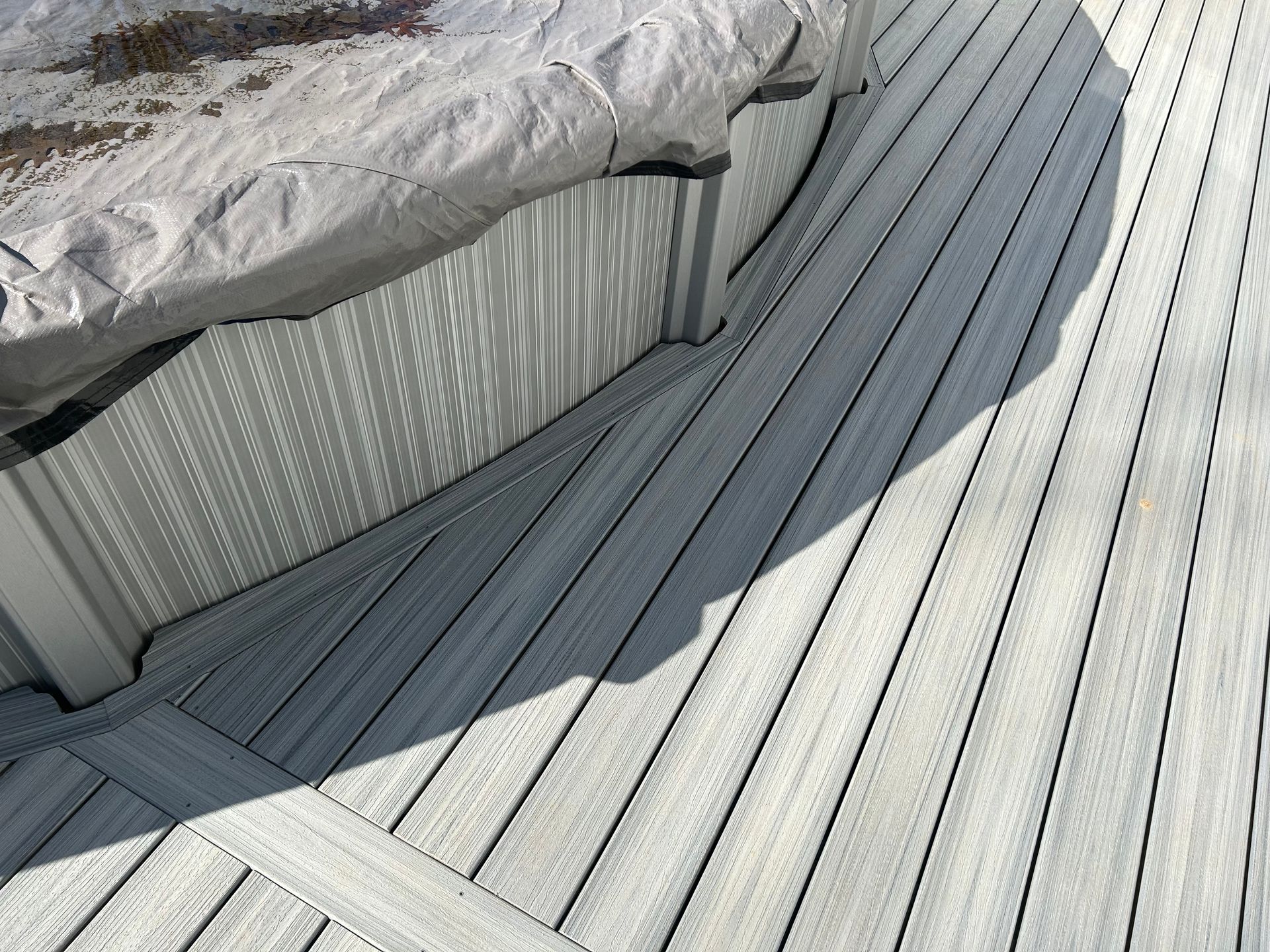 A light gray composite deck curves around a covered pool. Sunny conditions create shadows.