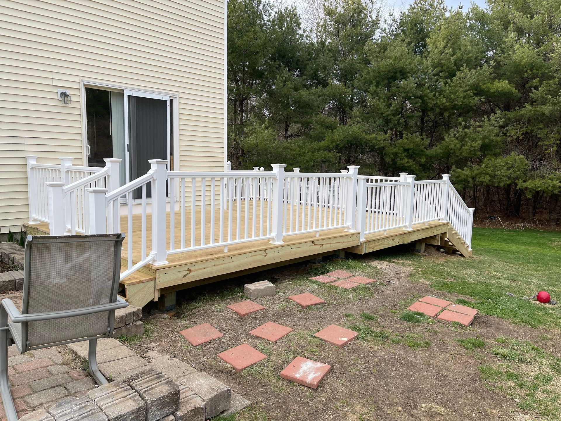 White deck with a ramp and stairs next to a beige house, surrounded by greenery.