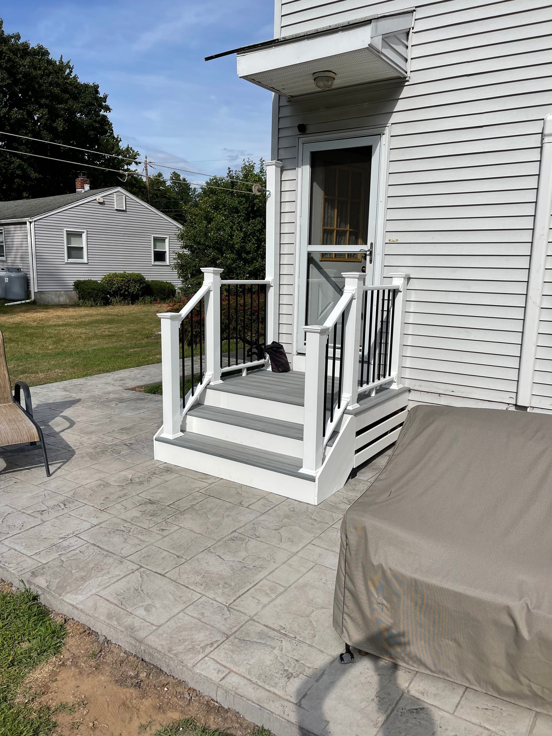 White porch steps with black railing leading to a door on a white house with a concrete patio.