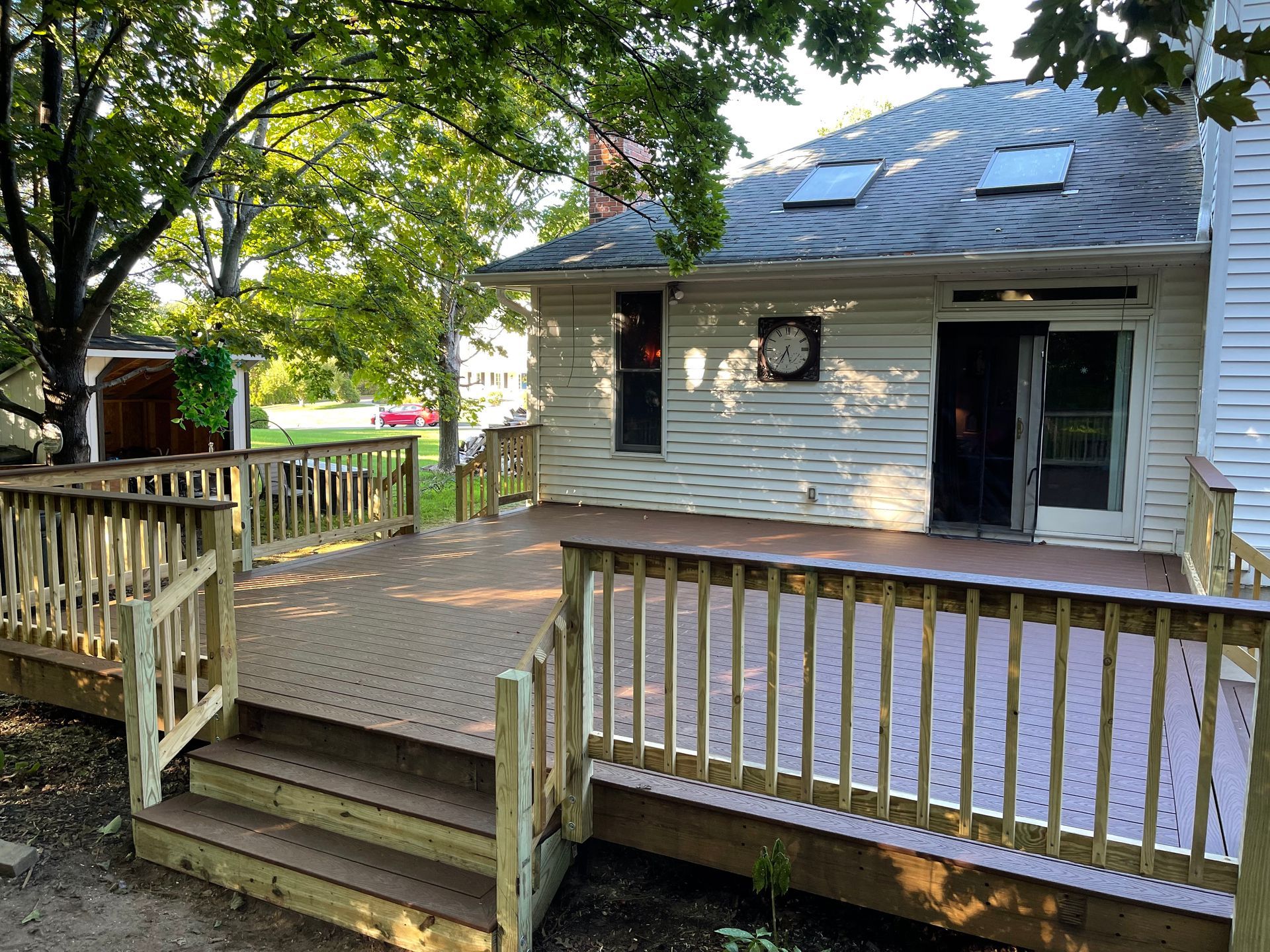 Composite deck with railing and ramp, attached to a white house with sliding glass doors, under a tree.