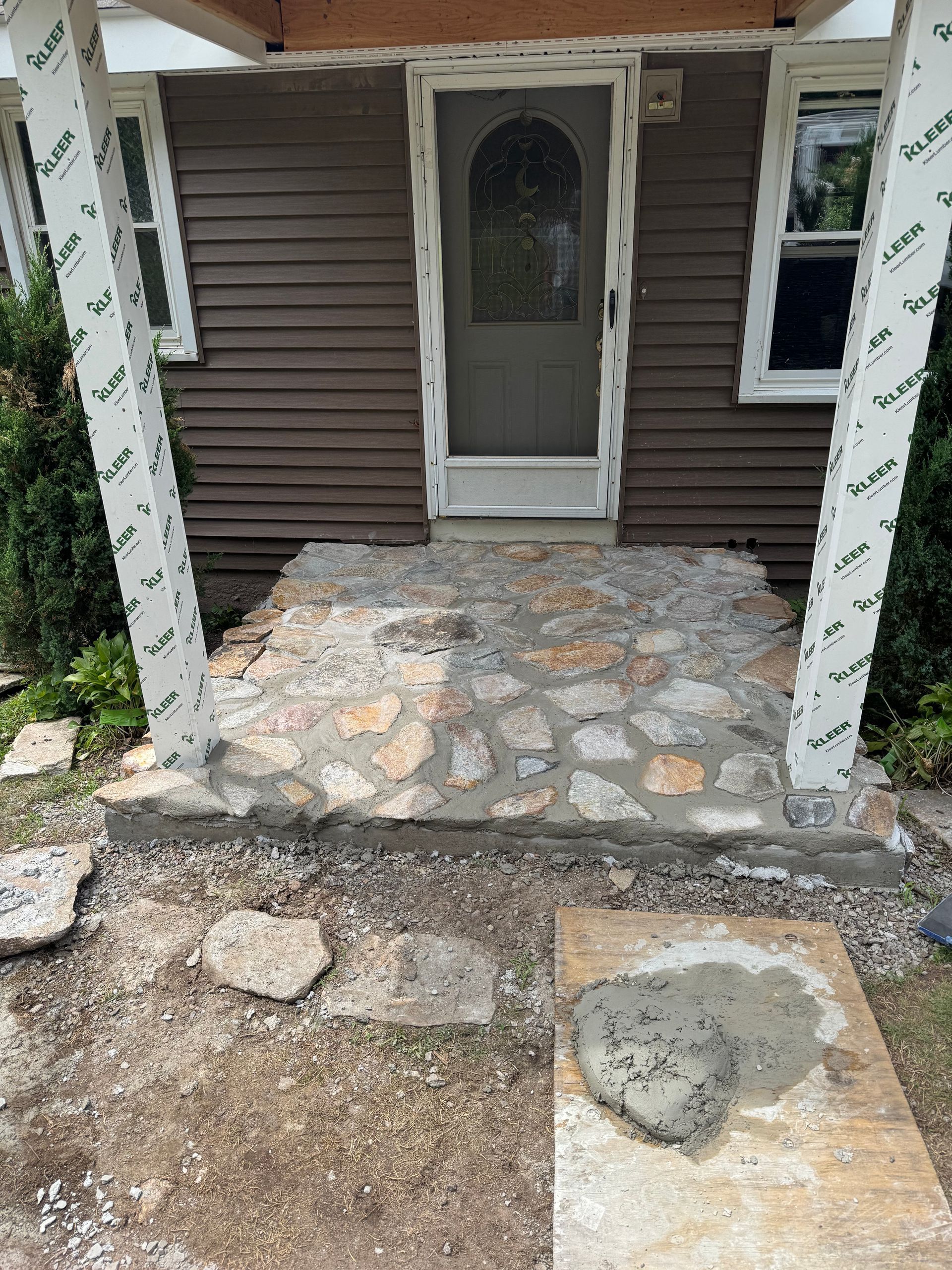Stone front porch under construction; entryway of brown house with white trim.