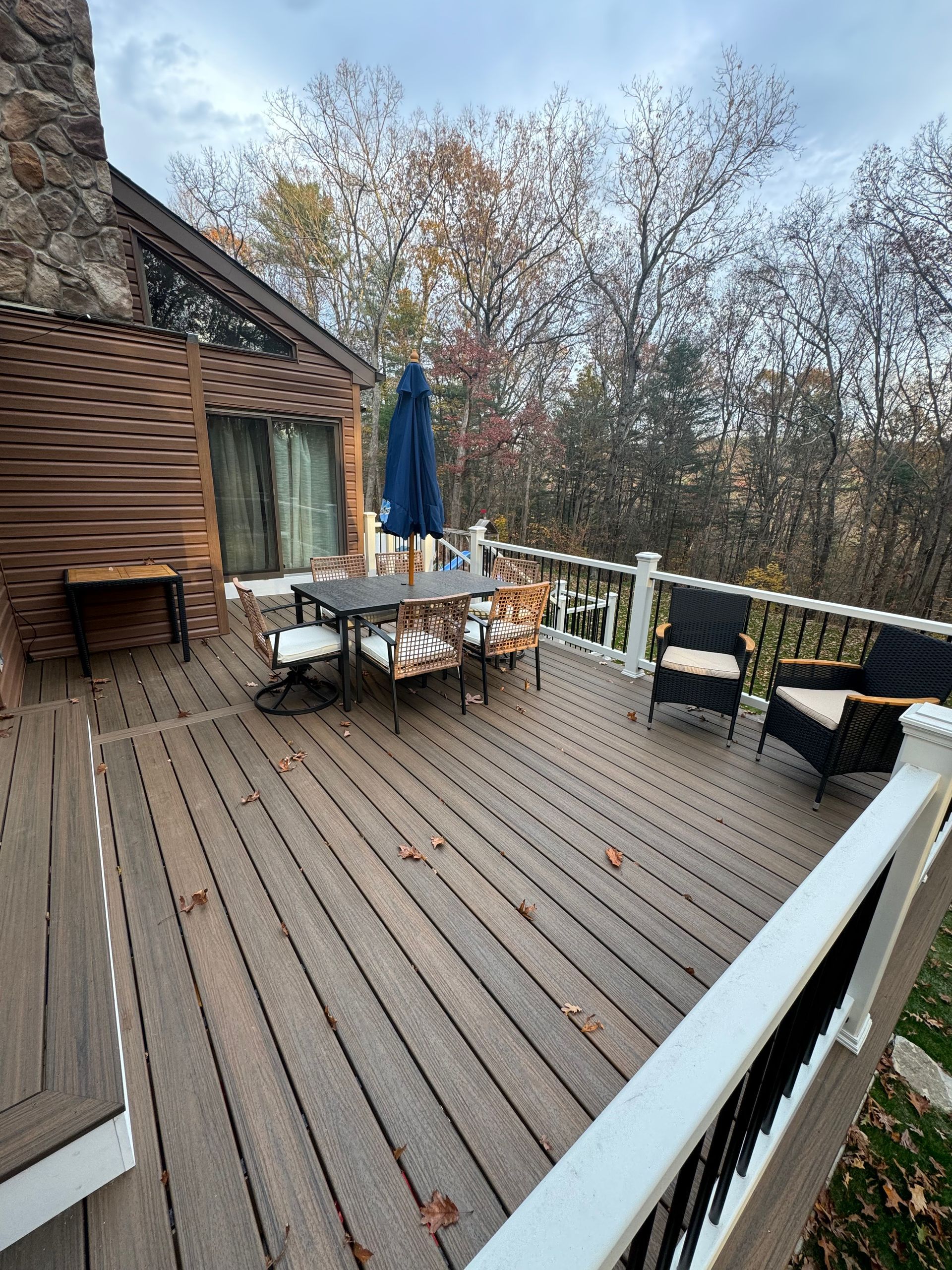 Wooden deck with outdoor furniture, surrounded by fall foliage, overcast sky.