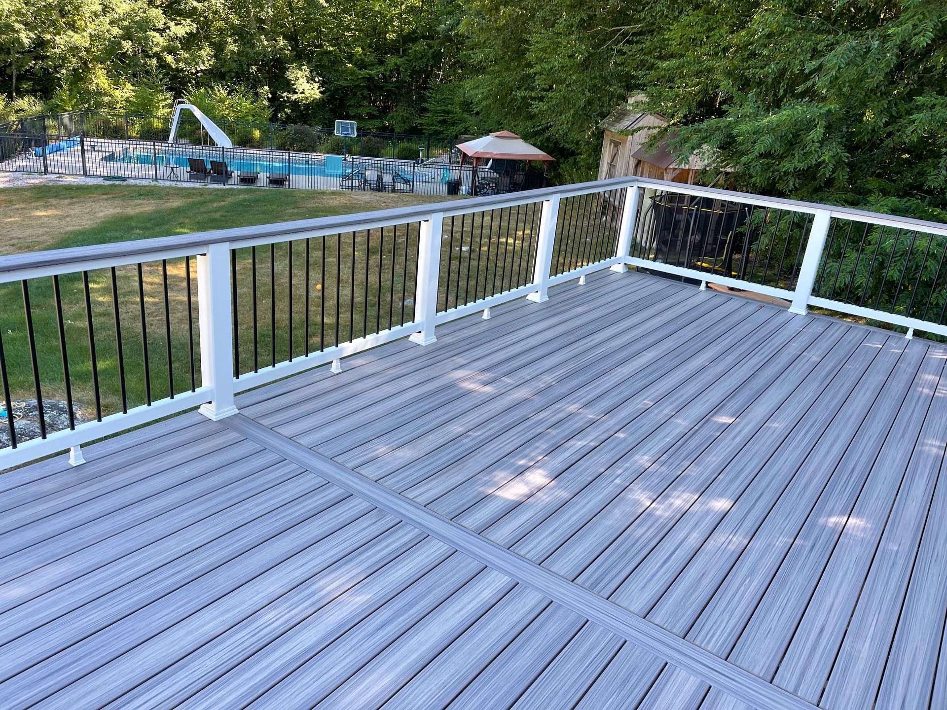Gray composite deck with white and black railings, overlooking a yard with a pool.
