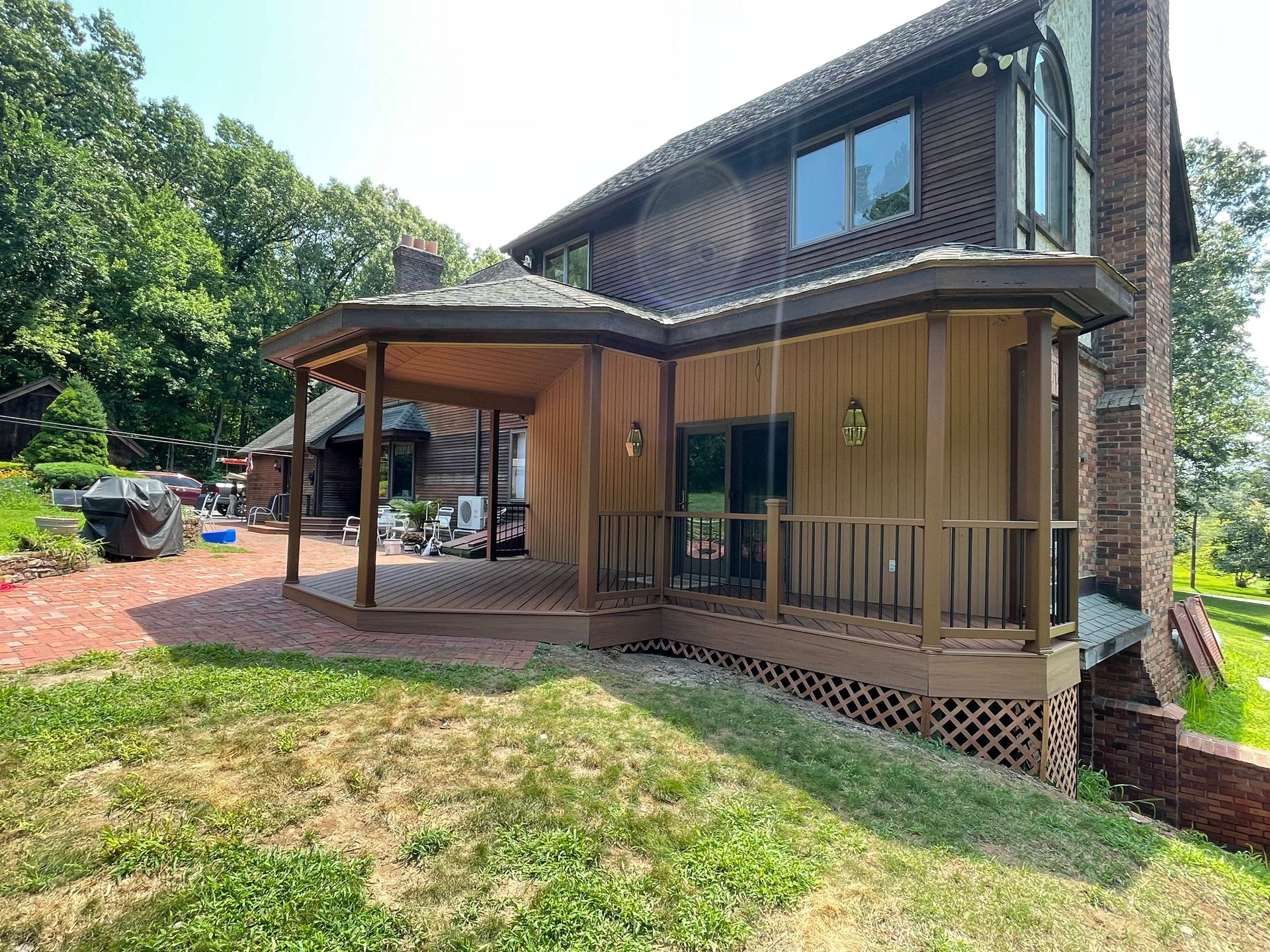 A two-story house with a brown exterior, a deck, and a patio on a sunny day.