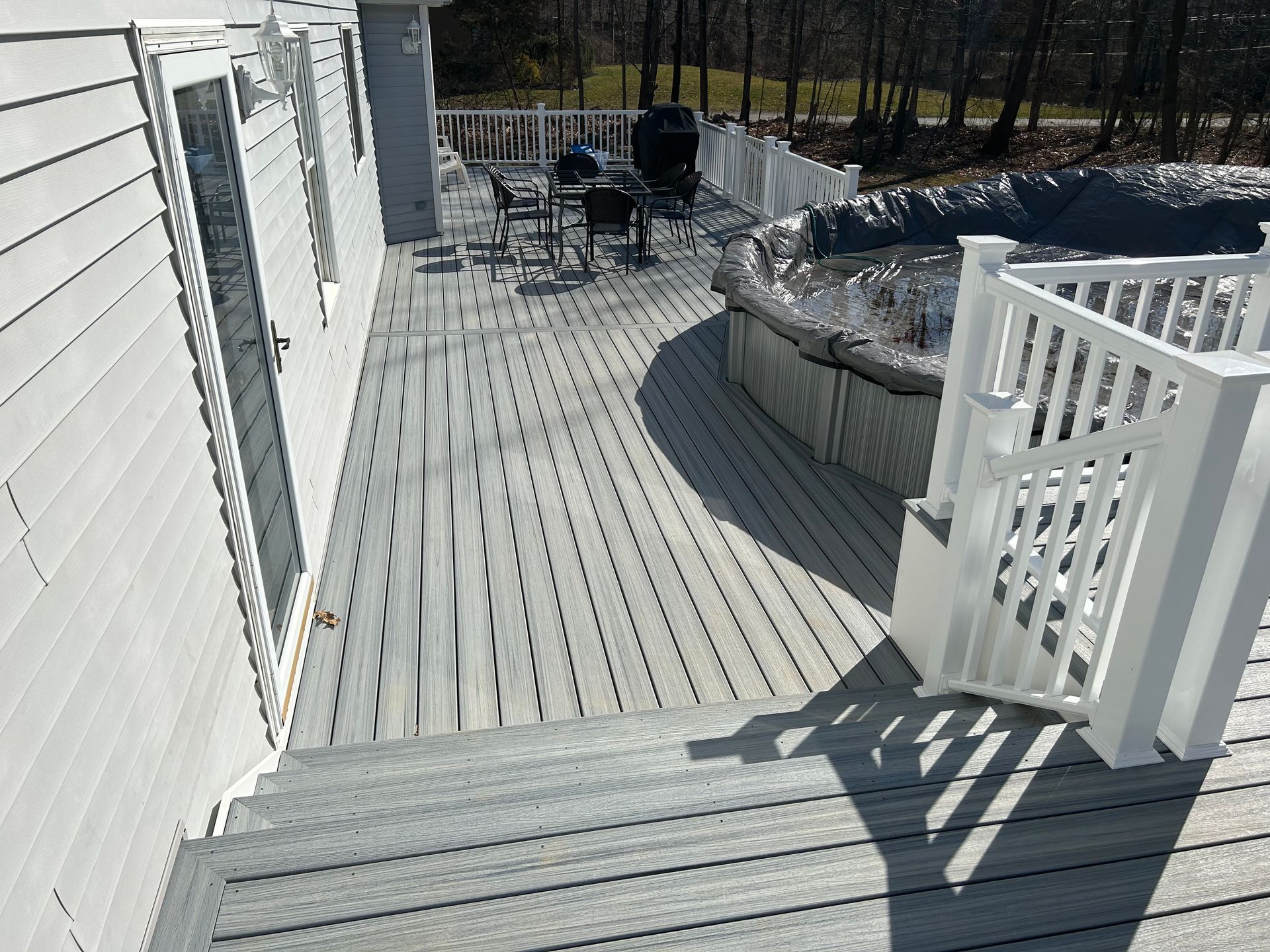 Gray composite deck with white railing, steps, and an above-ground pool, surrounded by trees.