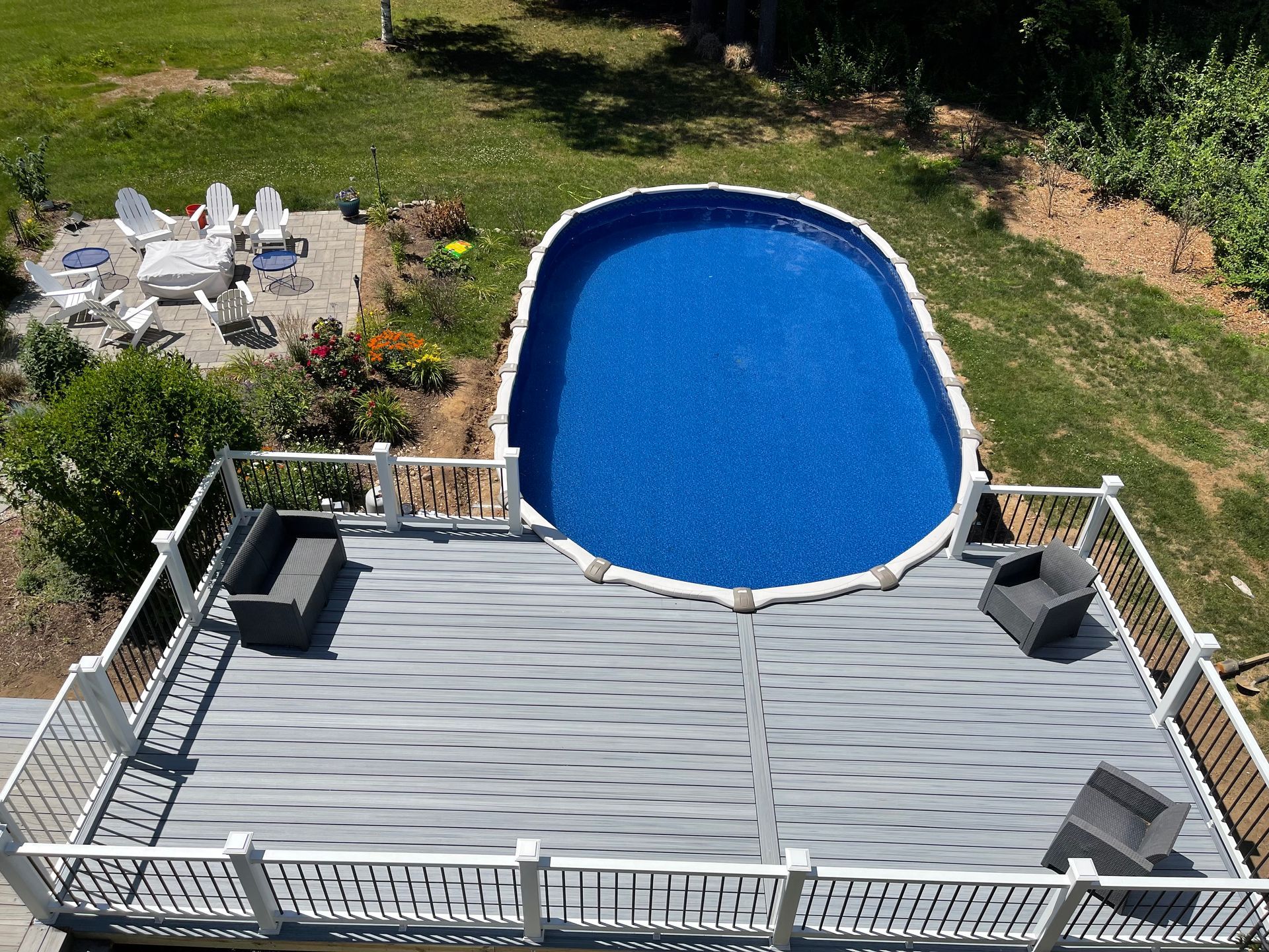 Overhead view of an oval swimming pool on a deck with seating areas and a grassy backyard.
