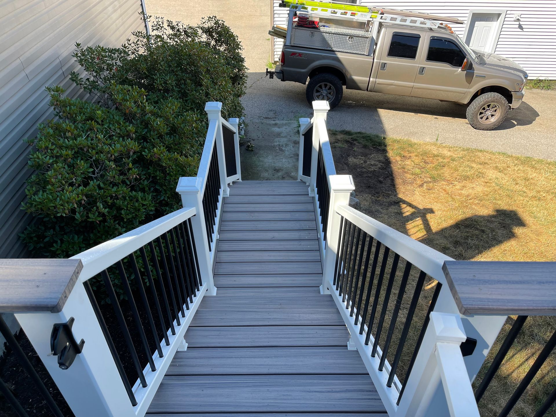 Outdoor staircase with white railing and black spindles leading down to a gravel driveway with a truck.