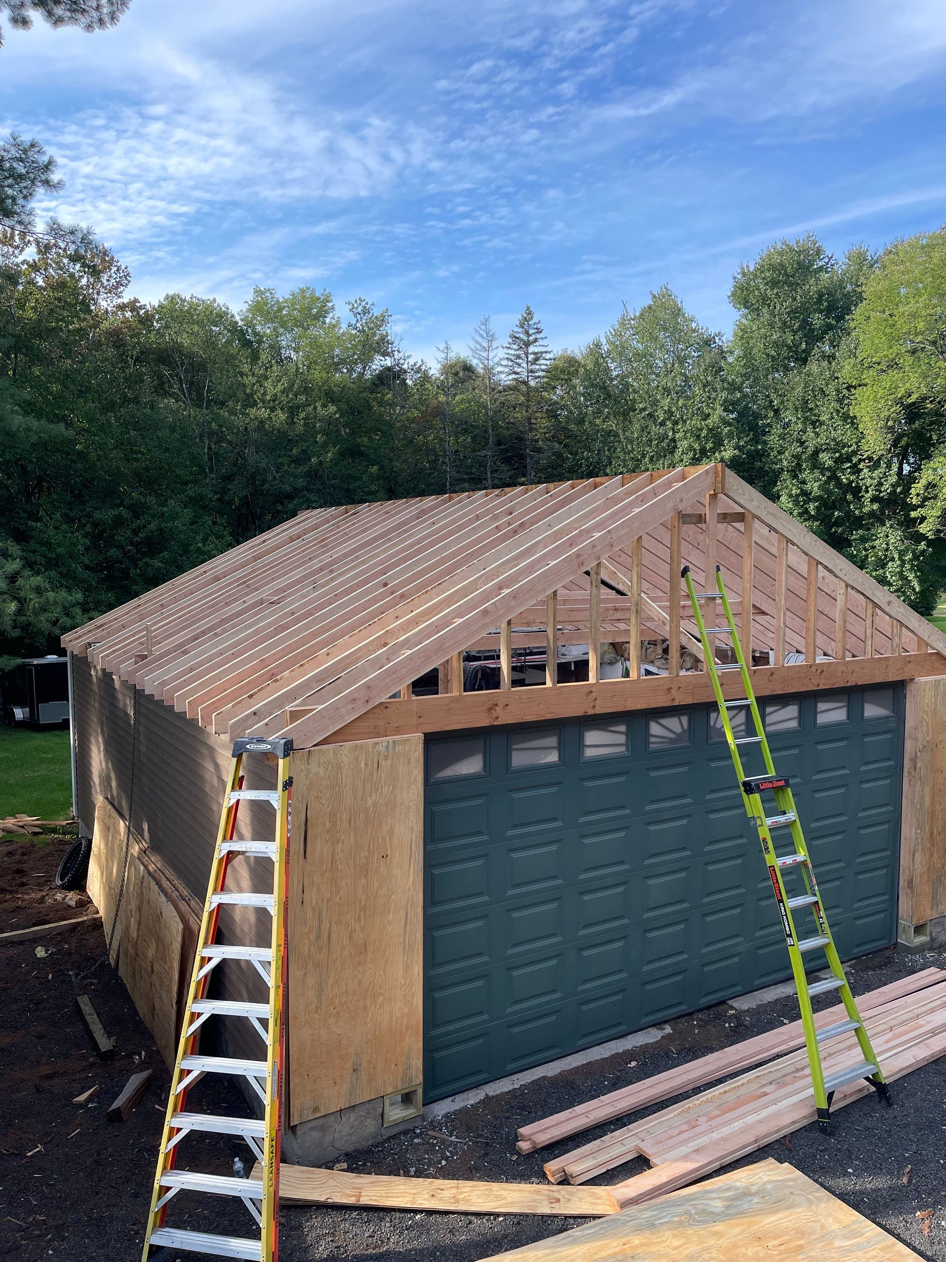 Garage under construction with green door, wood frame, and ladders outside.