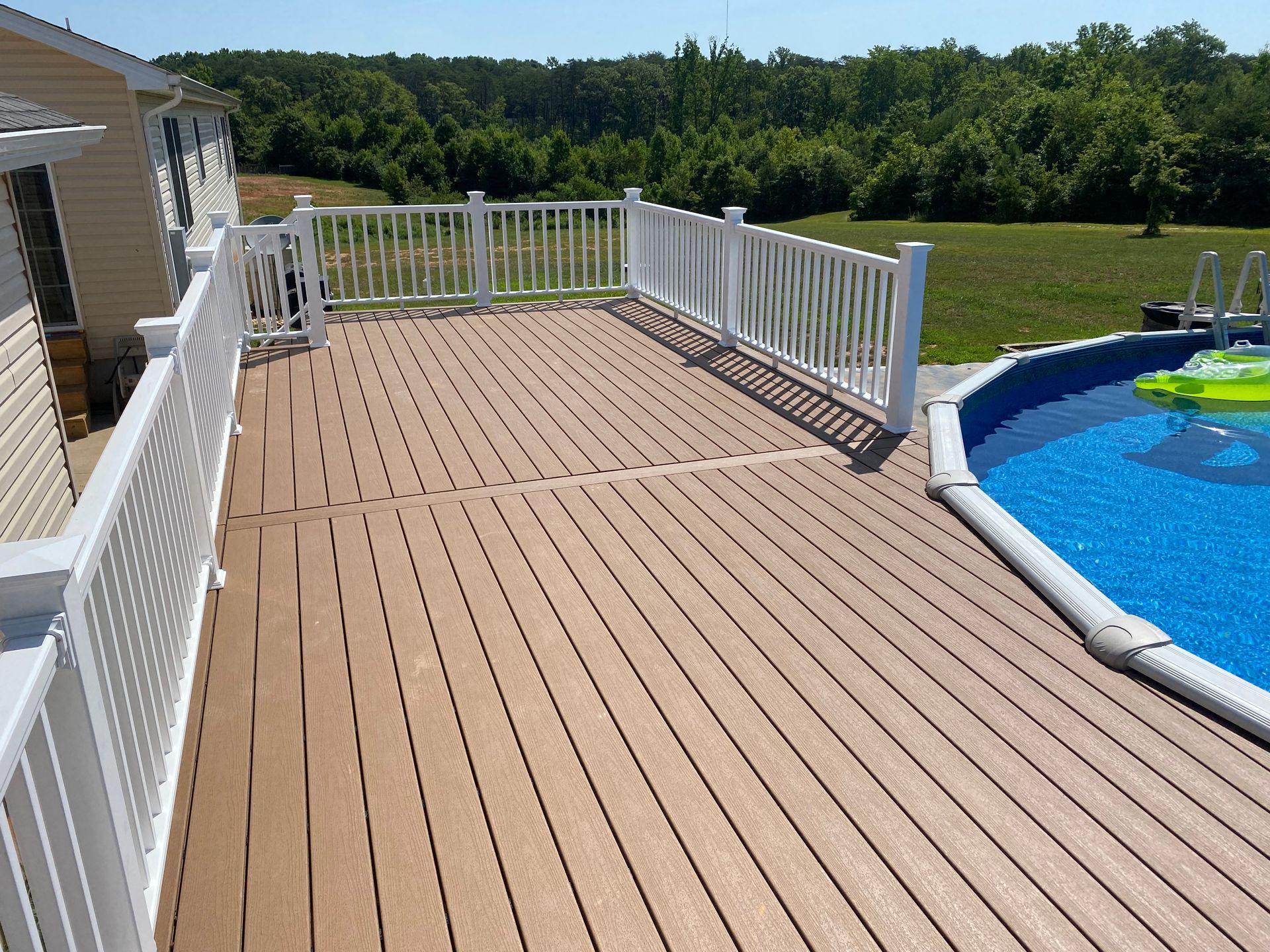 Brown deck with white railing next to an above-ground pool on a sunny day.