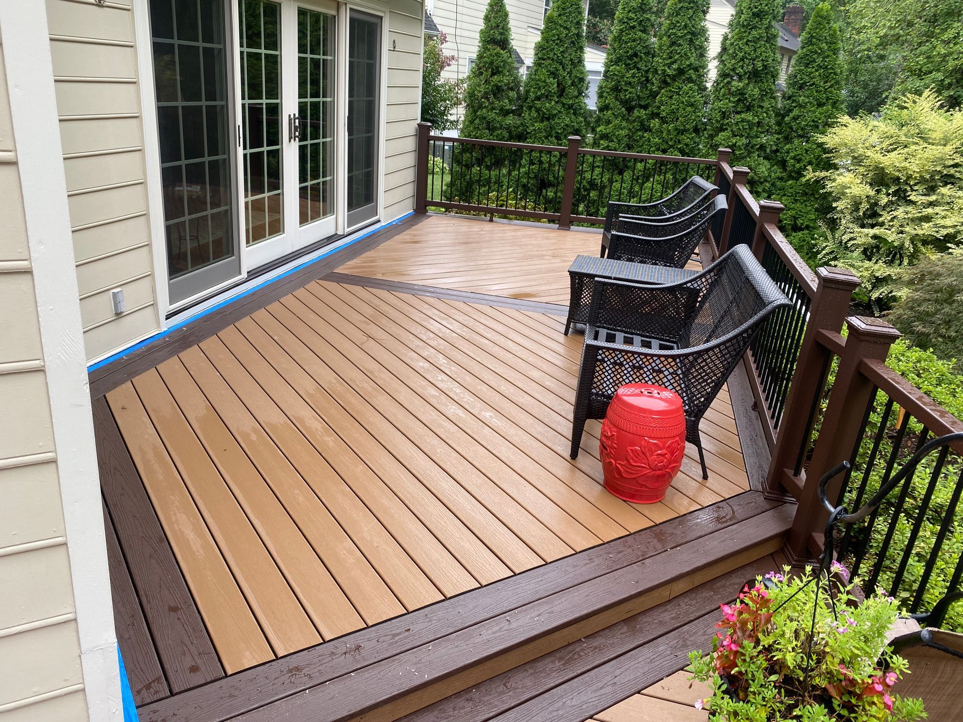 Composite deck with brown trim, two black chairs, red stool, and large sliding glass doors.