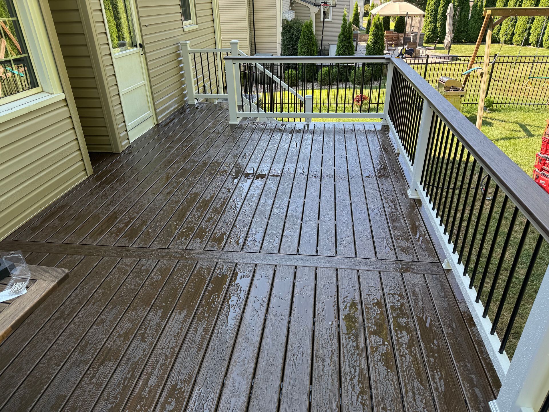 Wooden deck stained brown with black railings, overlooking a backyard with a swing set.