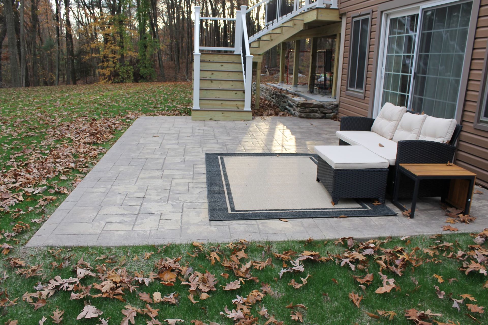 A patio with furniture and a rug next to a house, covered in fallen leaves.
