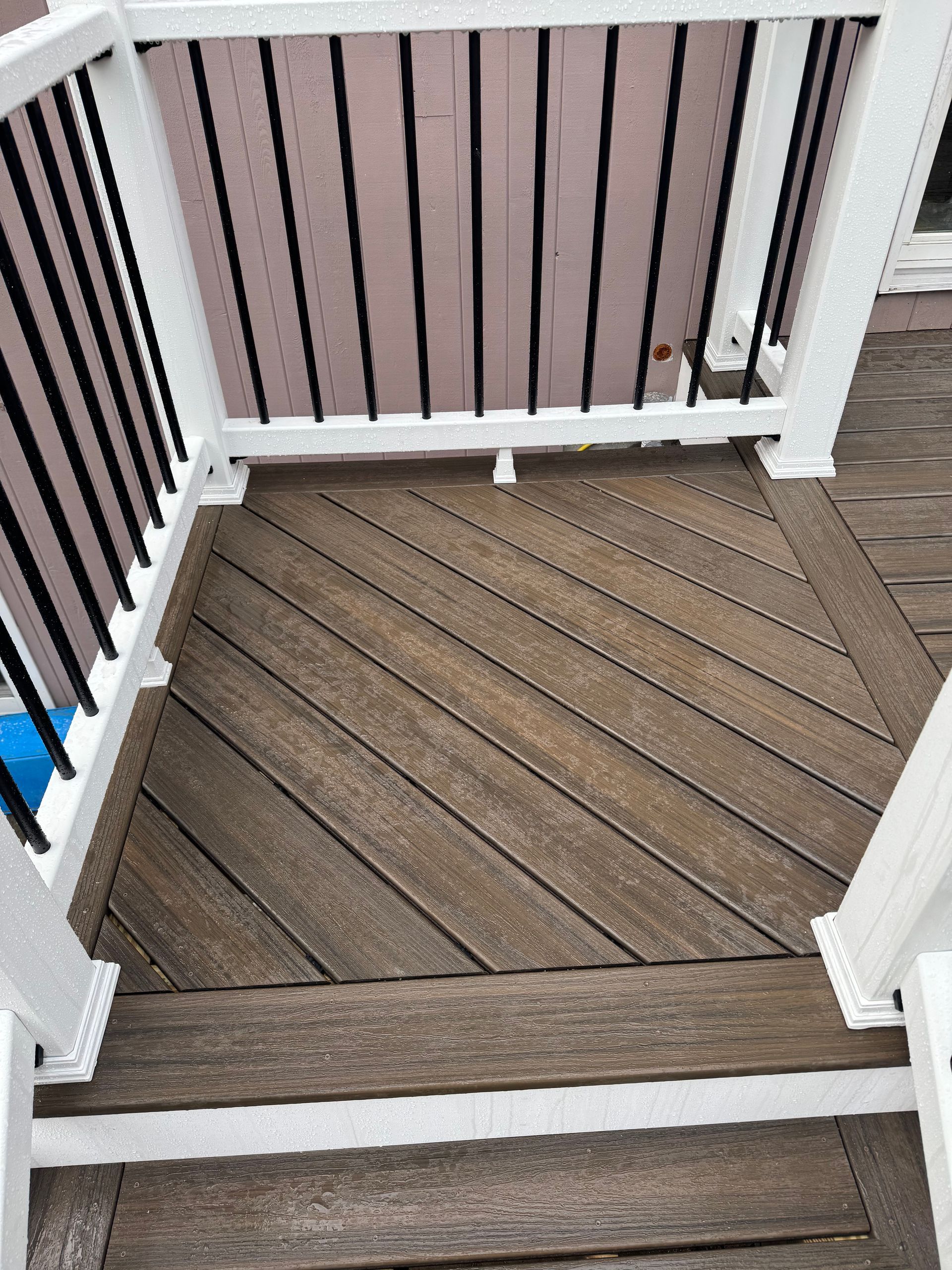 Wooden deck with diagonal planks, surrounded by white railings and black balusters.