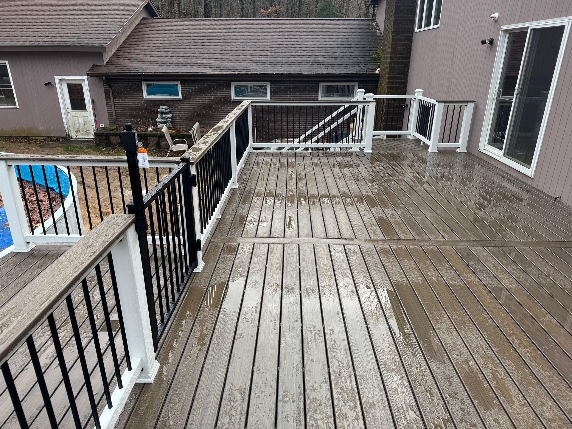 Wet, gray deck with black and white railings, near a pool and house.