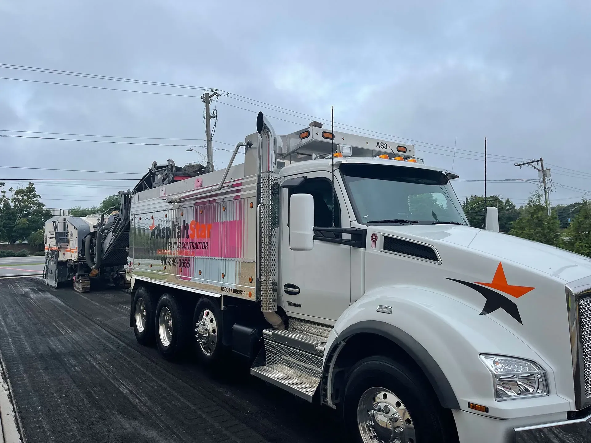 A white construction truck with an orange star logo parked on freshly paved black asphalt outdoors.