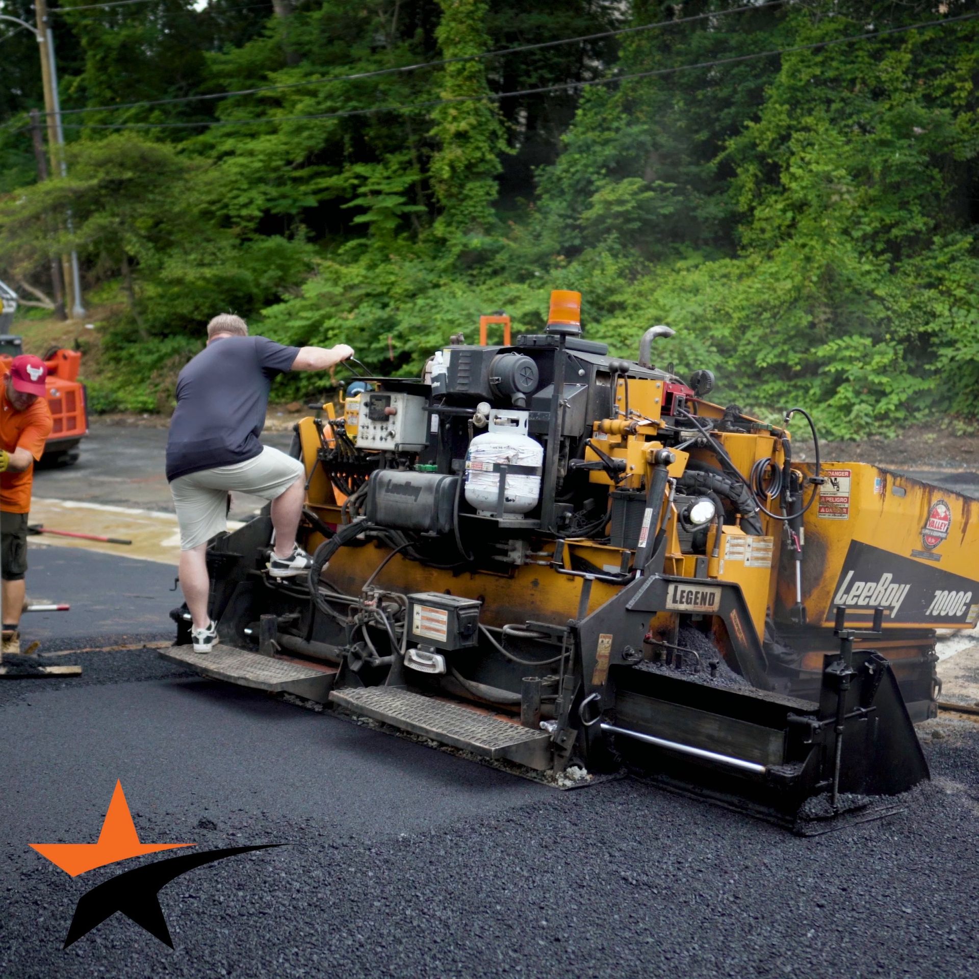 Workers operate a yellow LeeBoy asphalt paving machine on a construction site during a road paving project.