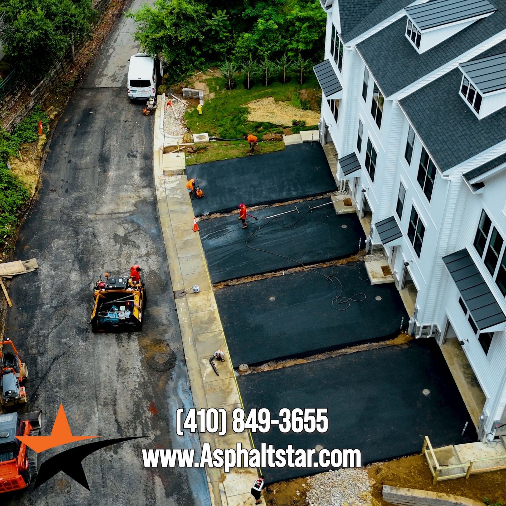 Aerial view of workers paving new driveways in front of a white residential townhome complex.