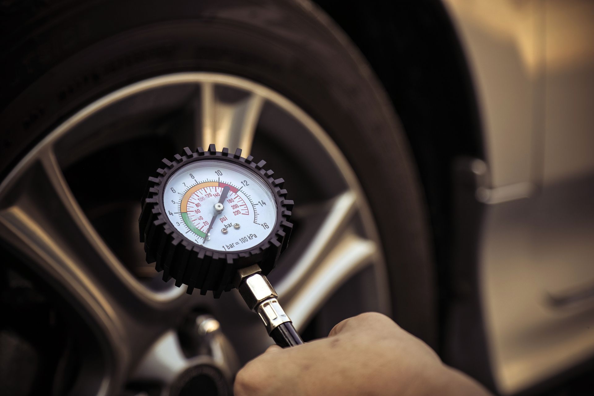 Handheld tire pressure gauge checking a car wheel’s valve stem