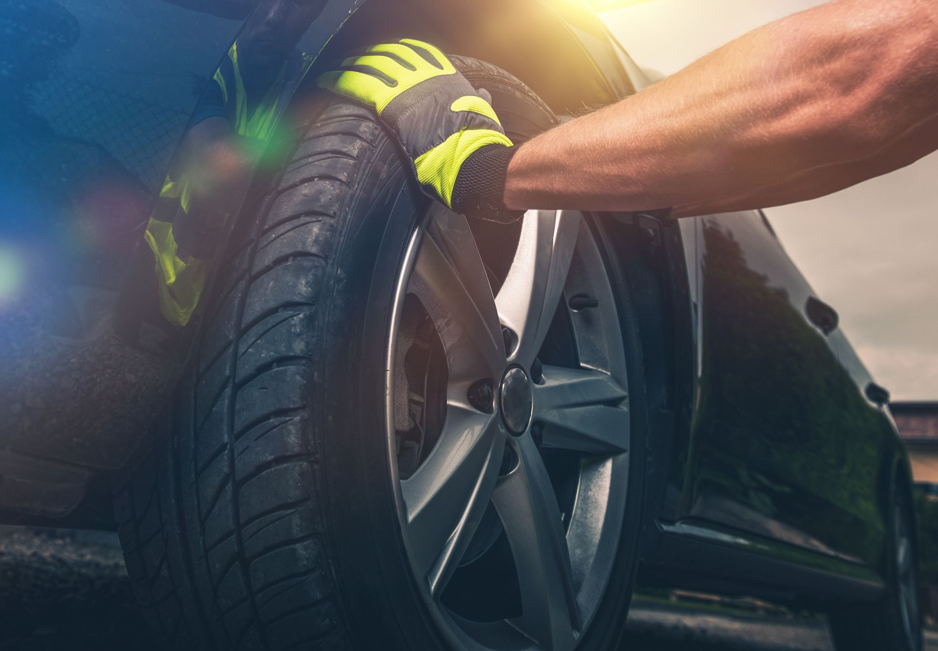 Gloved hands mounting a car tire onto a wheel rim in a garage
