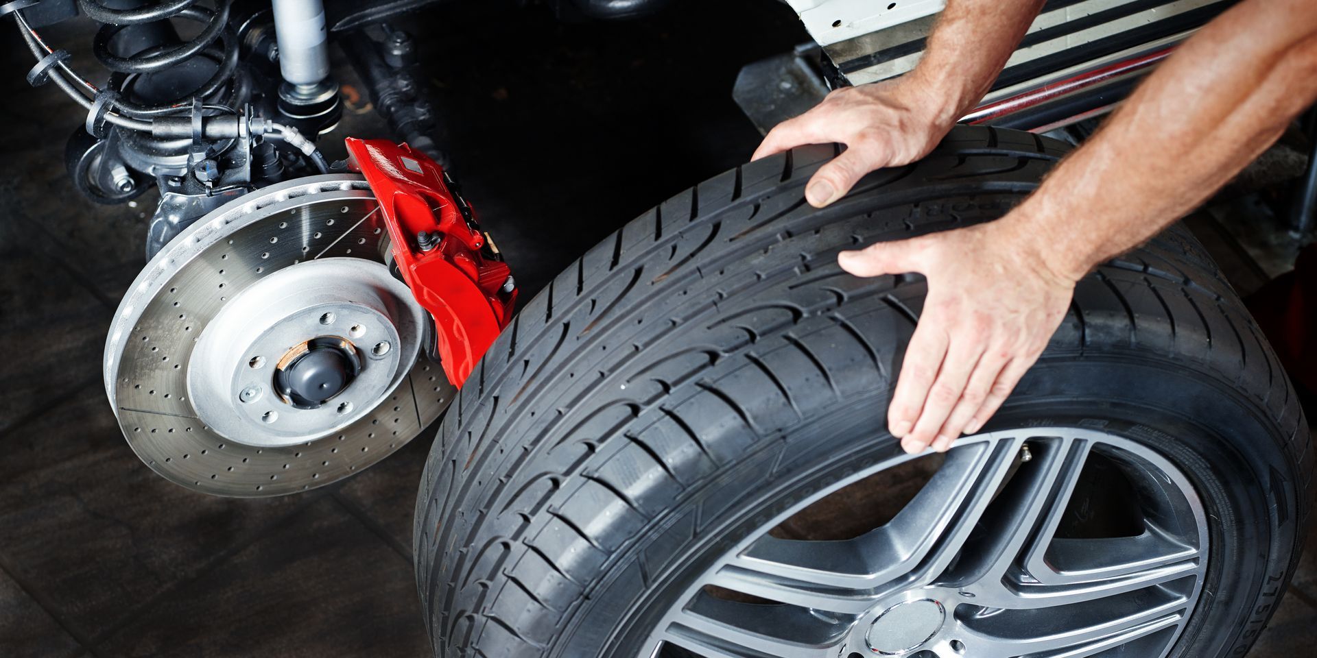 Mechanic installing a new car tire with a red brake caliper visible
