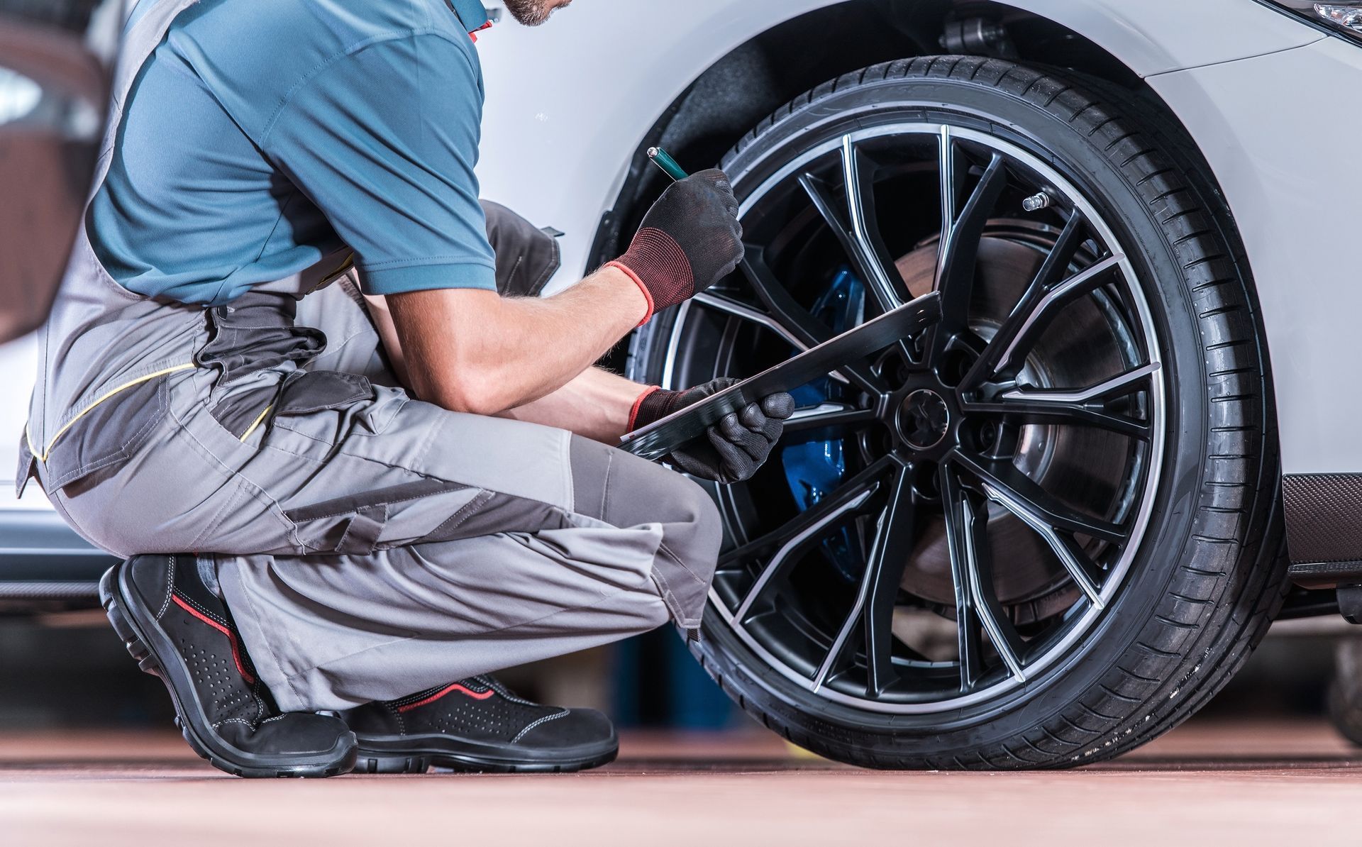 Mechanic using a ratchet on a black car wheel during tire service, crouched beside the vehicle.