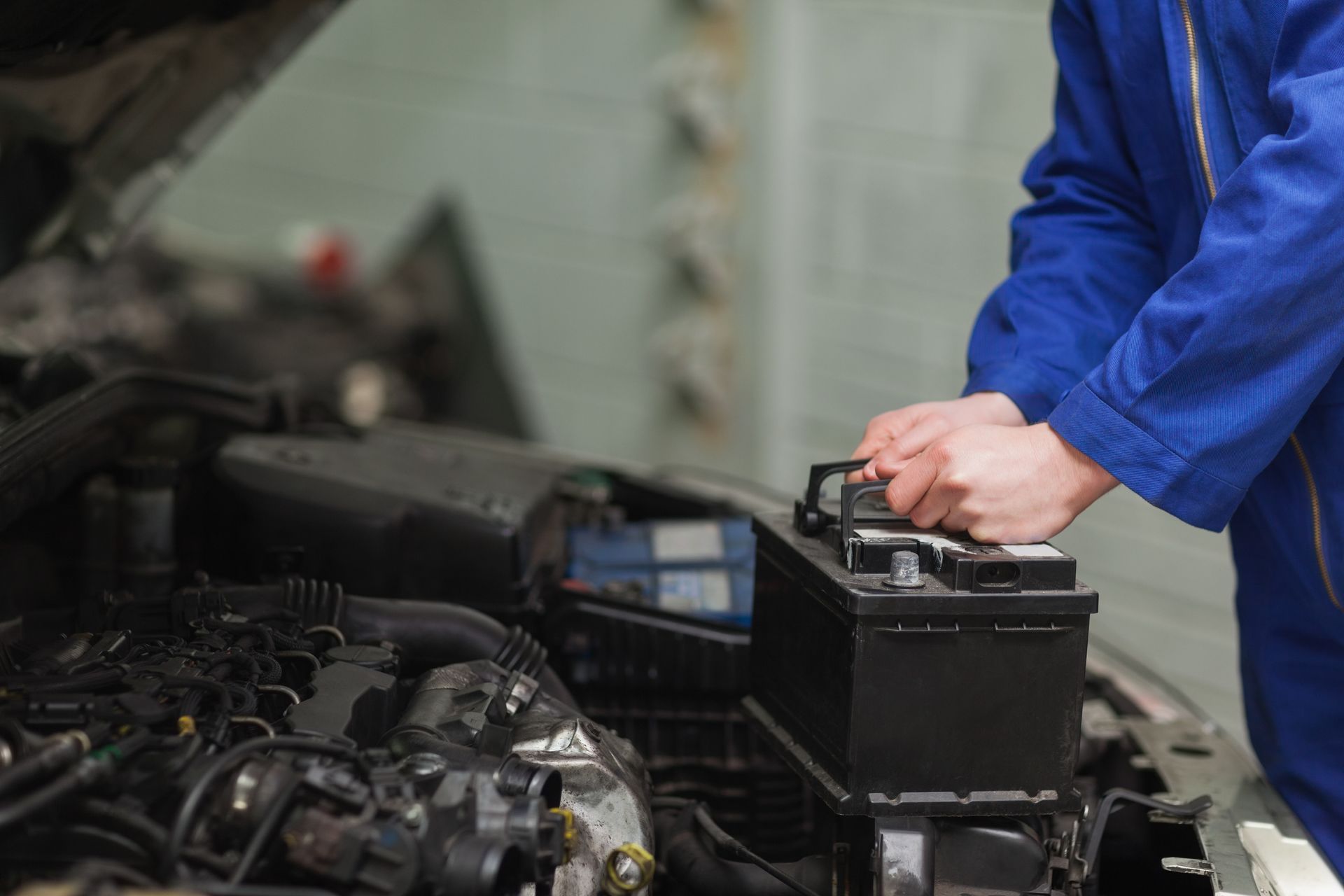 Mechanic in blue coveralls checking a car battery in an auto repair shop