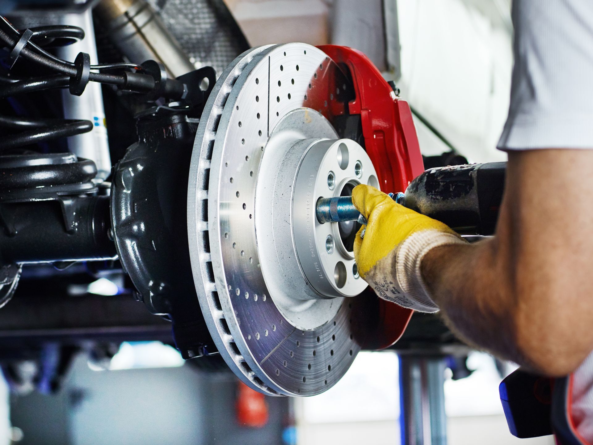 Mechanic installing a brake rotor on a car, wearing yellow gloves in an auto repair shop