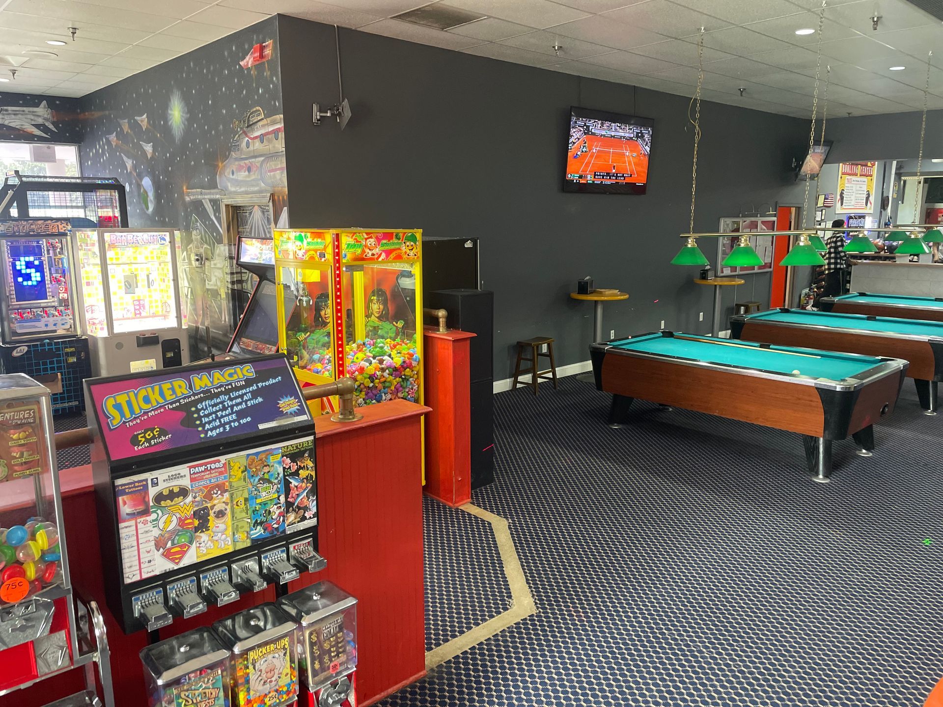 A game room with pool tables, arcade games, and a candy machine