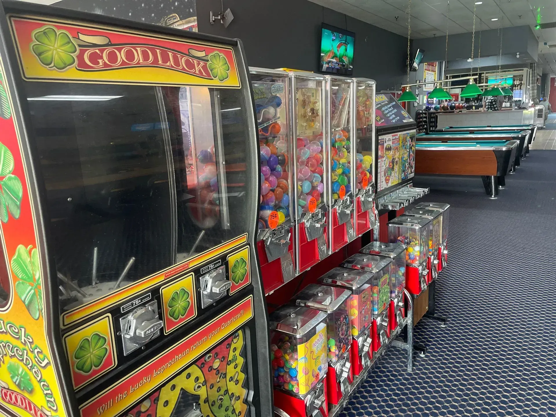 A row of gumball machines are lined up in a room with pool tables